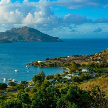 A coastal landscape with a view of the sea, boats, and a small settlement with houses and greenery.