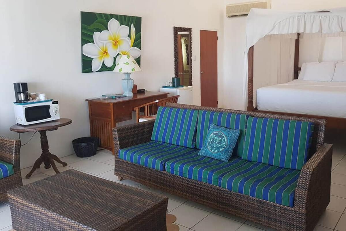 A hotel room with a bed, a sofa, a small table with a microwave, a chair, and a painting of flowers on the wall.