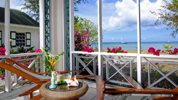 A covered outdoor area with a view of the sea, featuring a table with books and a decorative item. - Oualie Beach Resort (Newcastle)