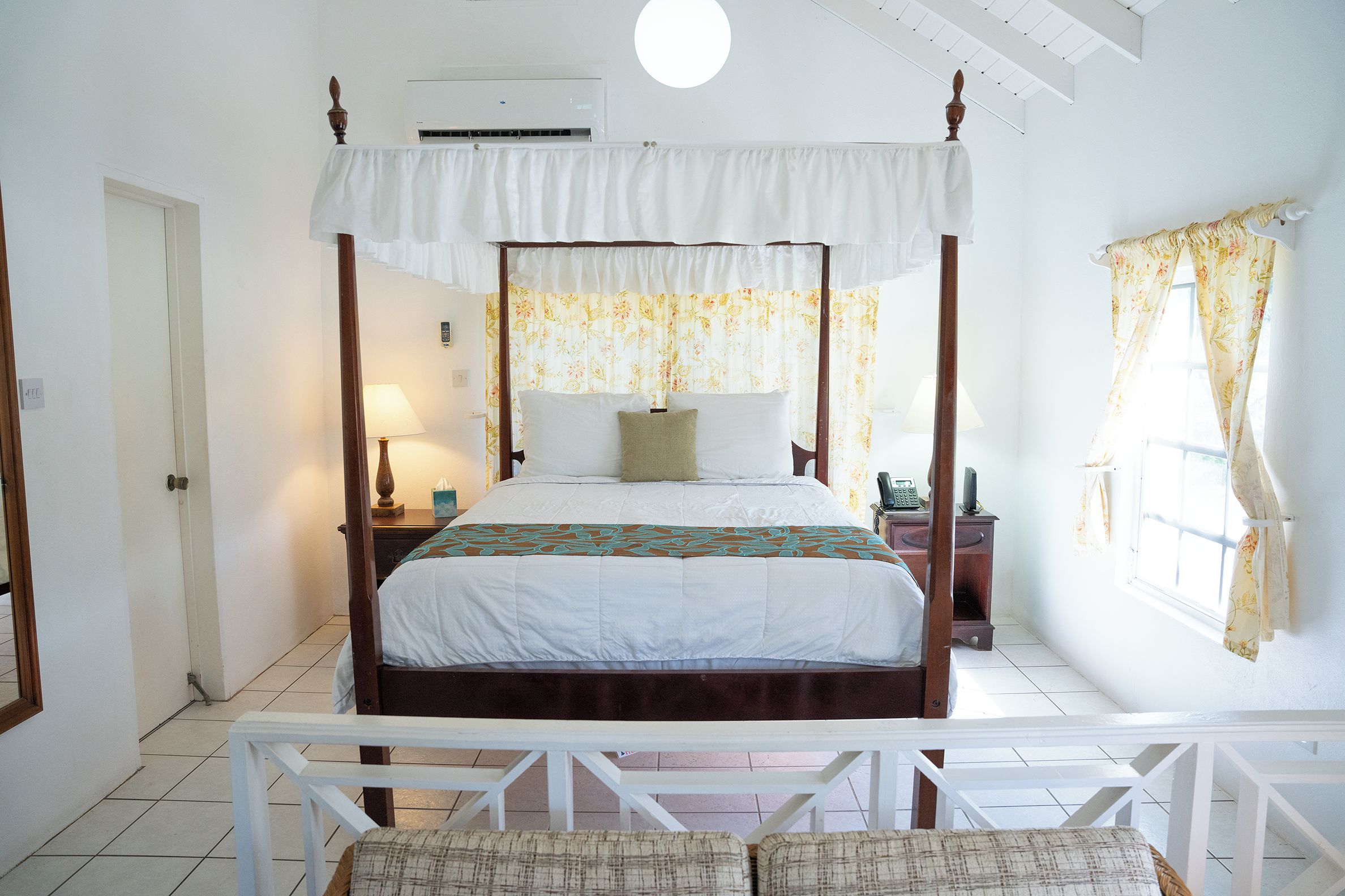Una camera da letto con un letto a baldacchino, un comodino con una lampada, una finestra con tende e una porta.