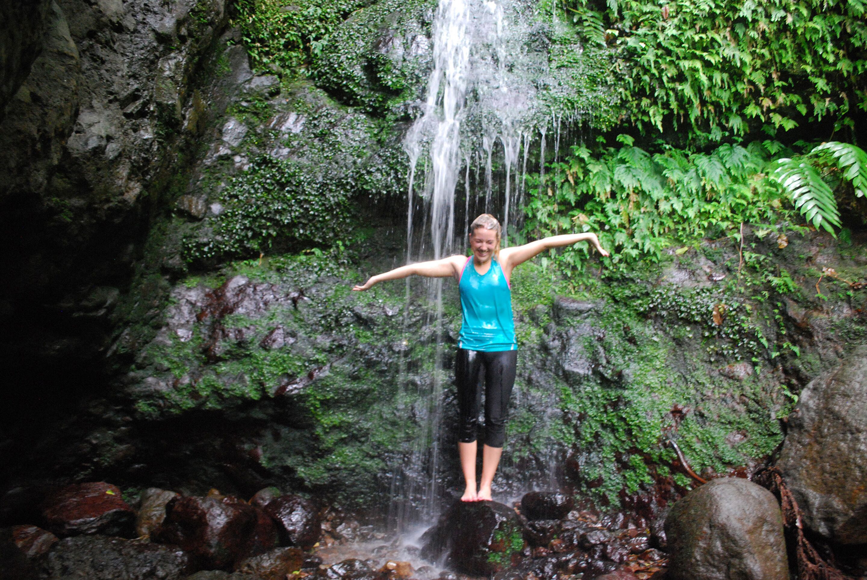 A person standing on a rock with arms outstretched in front of a waterfall.
