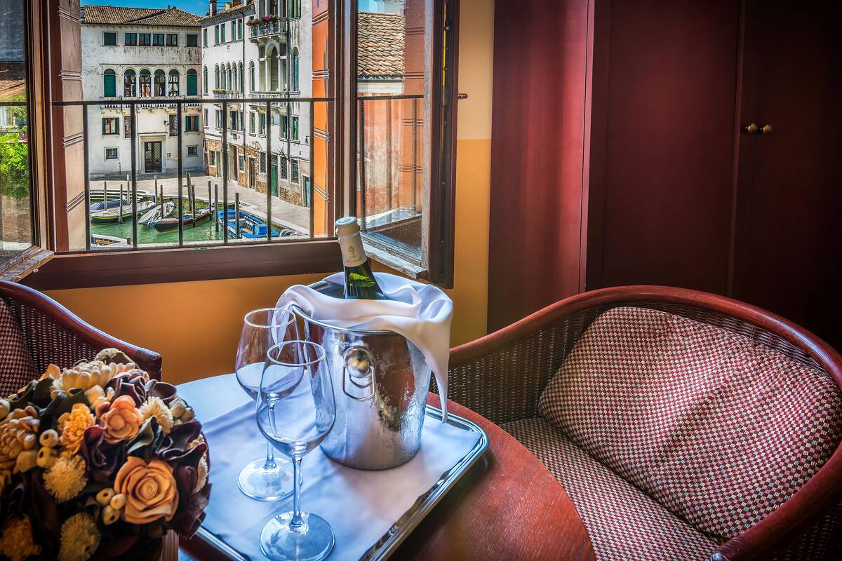 A room with a view of Venice through a window, a tray with a bottle of champagne, glasses, and a bouquet of flowers.