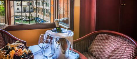A room with a view of Venice through a window, a tray with a bottle of champagne, glasses, and a bouquet of flowers.
