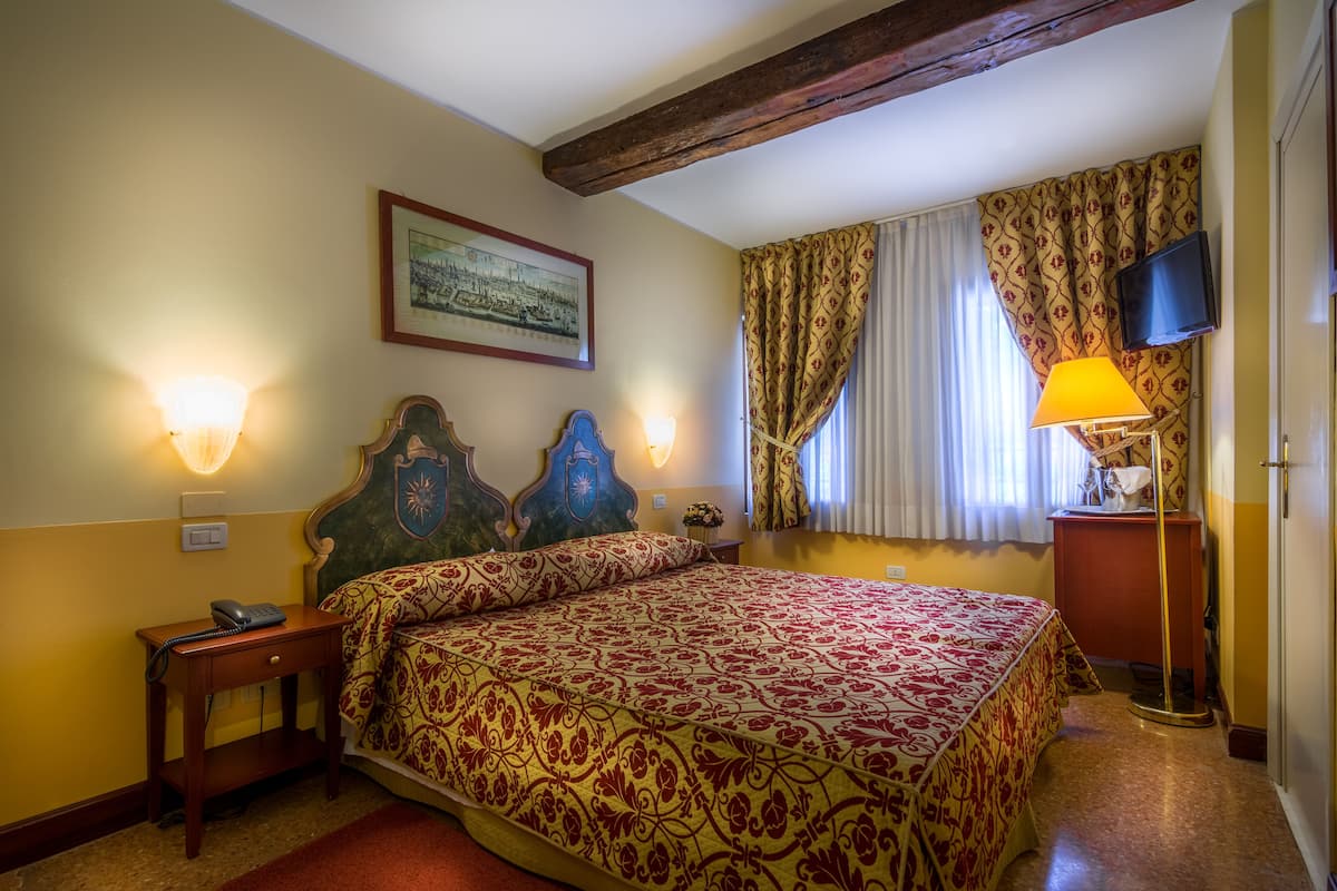 A hotel room with a bed, two wall-mounted lamps, a framed picture, a television, and a telephone on a nightstand.