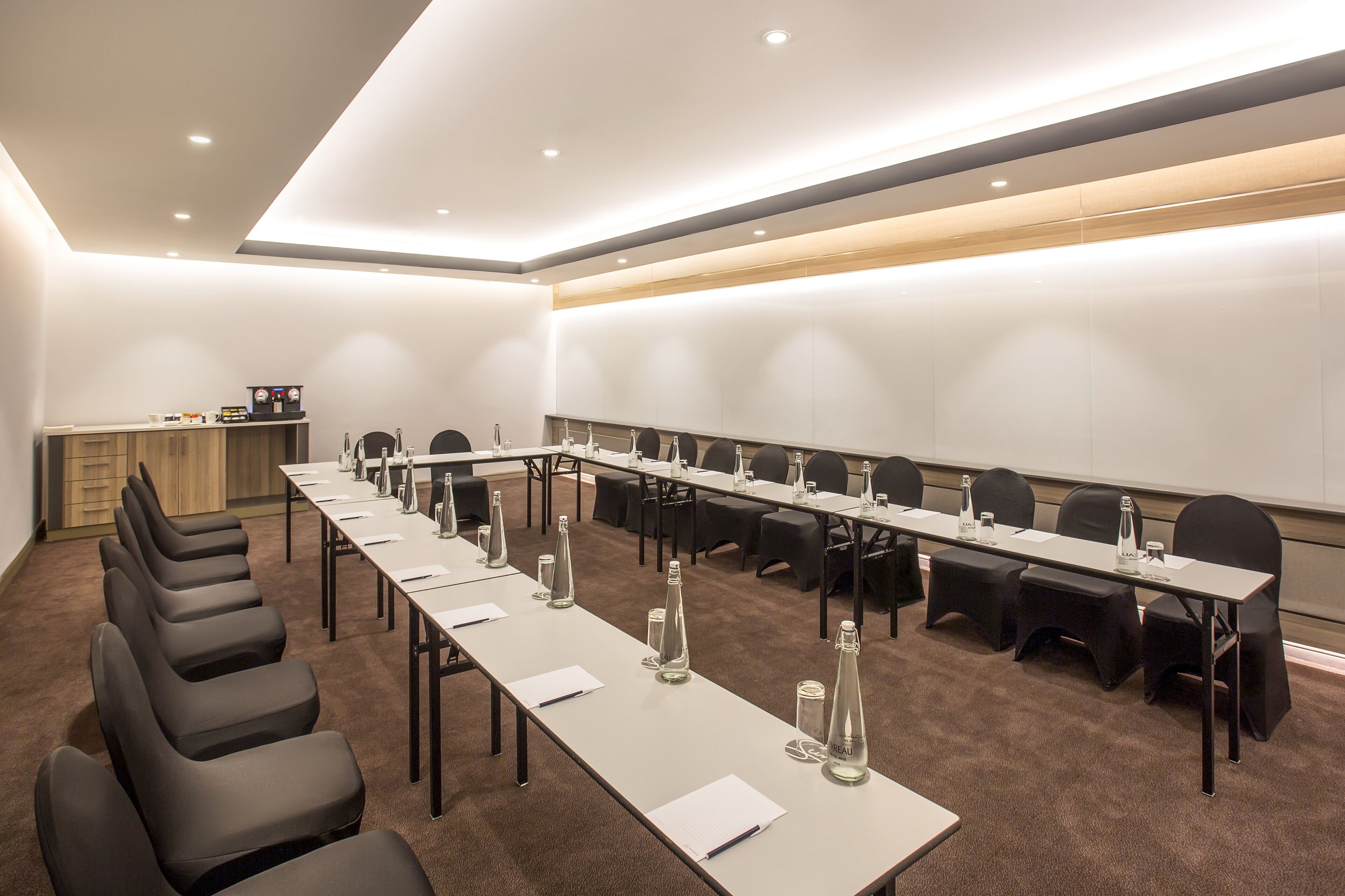 Uma sala de conferências com uma mesa comprida, cadeiras e garrafas de água.