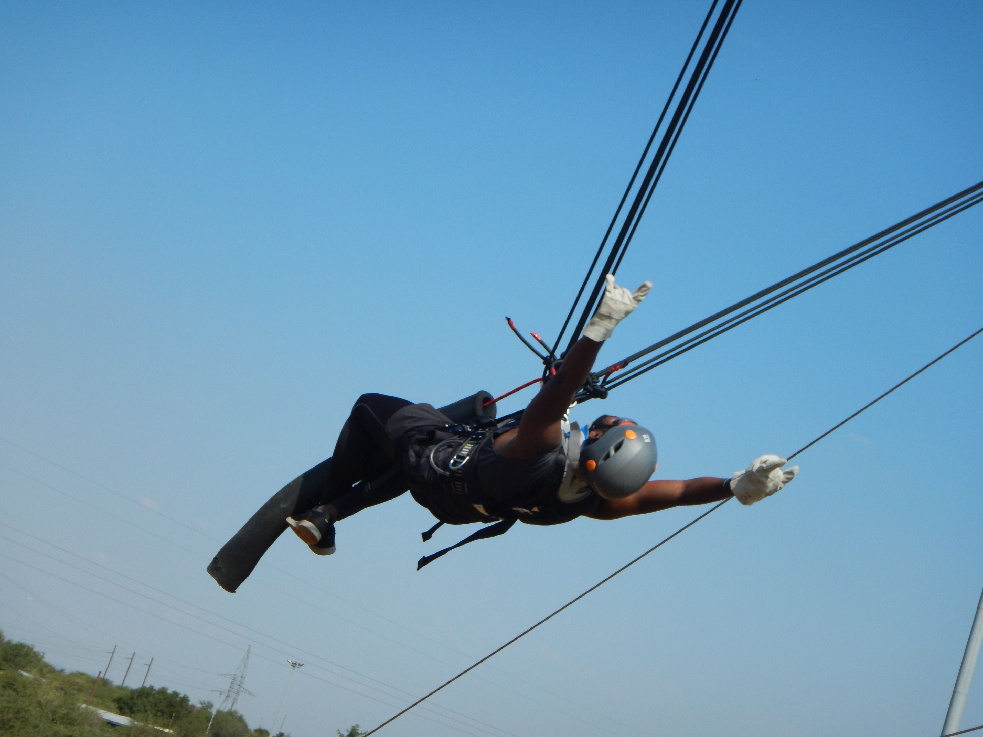 Una persona haciendo parapente con arnés y casco, suspendida por cuerdas contra un cielo despejado.