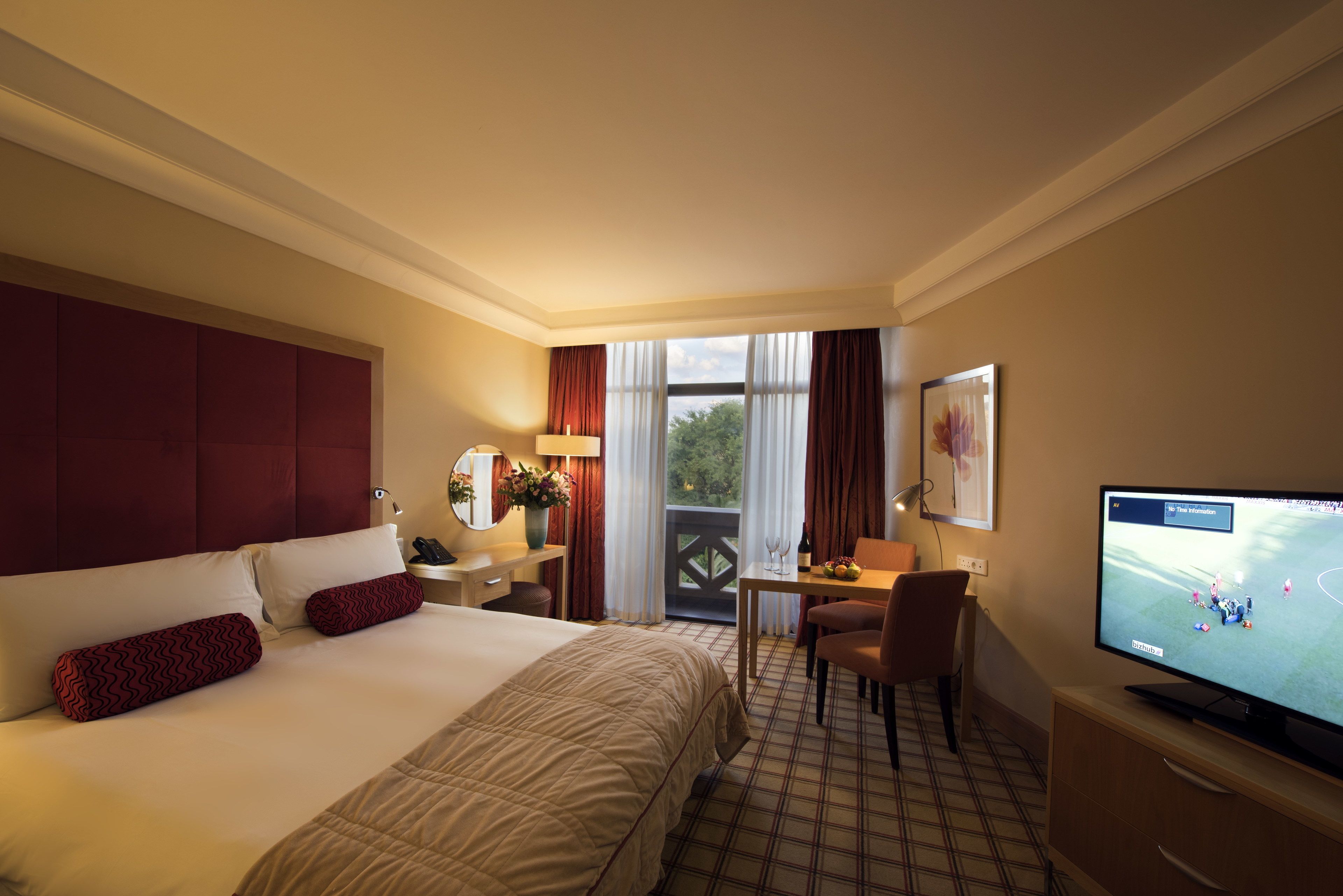 A hotel room with a bed, a desk, a television, and a view of the outdoors.