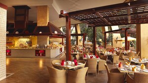 A spacious restaurant with wicker chairs and tables, a central bar, and a view of the outdoors. - Sun City Hotel and Casino (Moses Kotane)