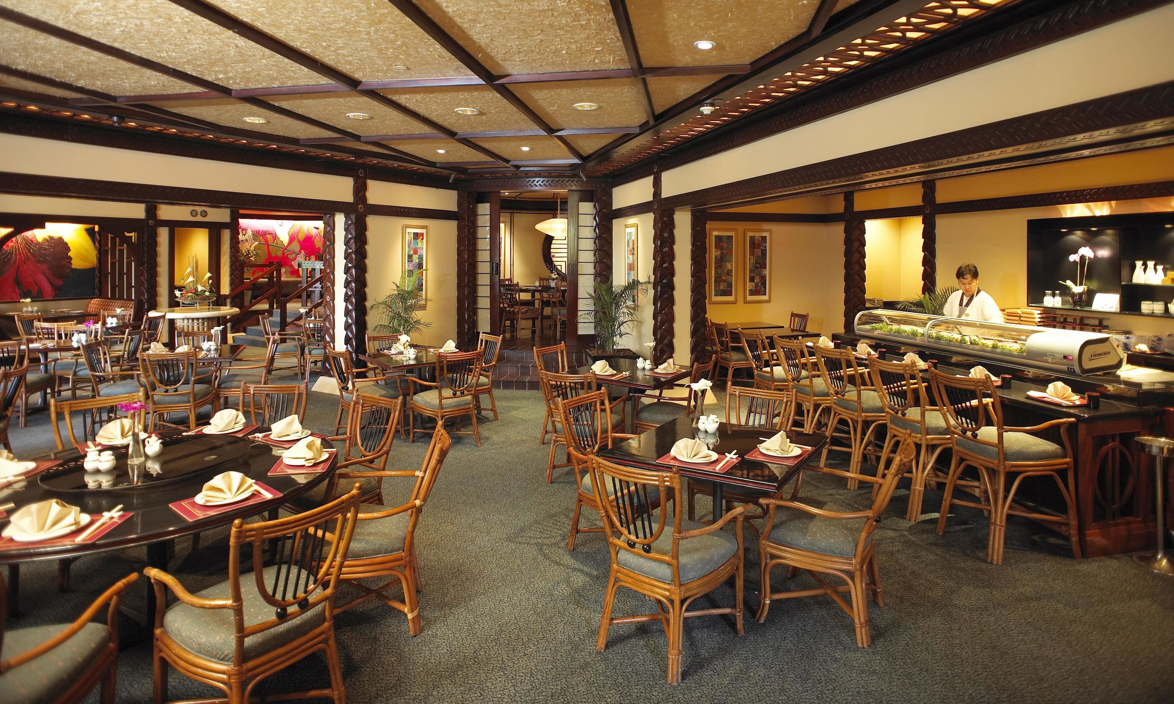 A restaurant with multiple dining tables and chairs, a central serving area, and a decorative ceiling.