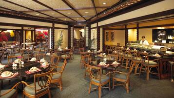 A restaurant with multiple dining tables and chairs, a central serving area, and a decorative ceiling.