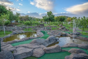Um campo de golfe com lago, grama artificial verde e pedras grandes.
