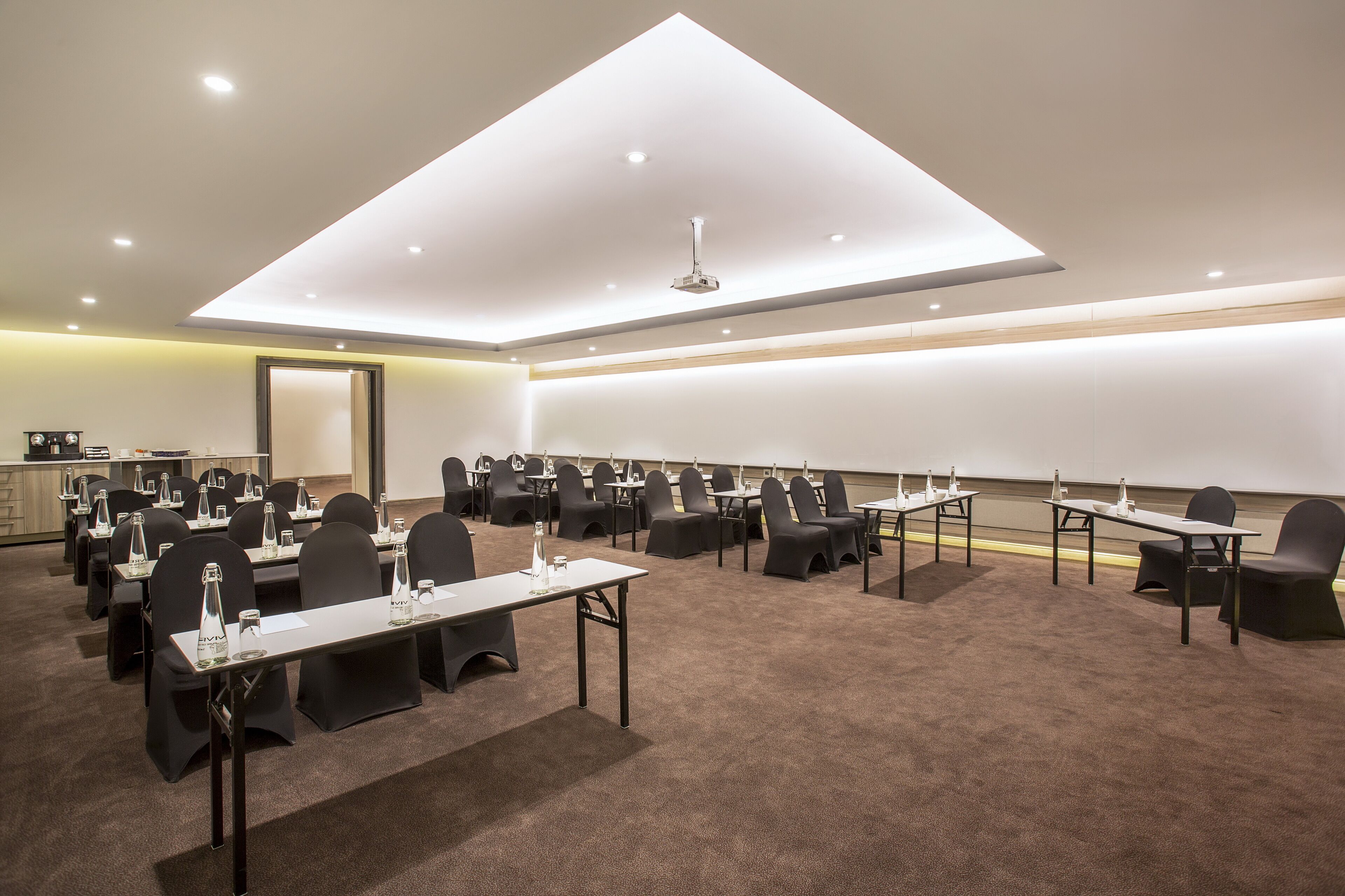 A conference room with multiple tables and chairs, equipped with water bottles and nameplates, and a ceiling light fixture.