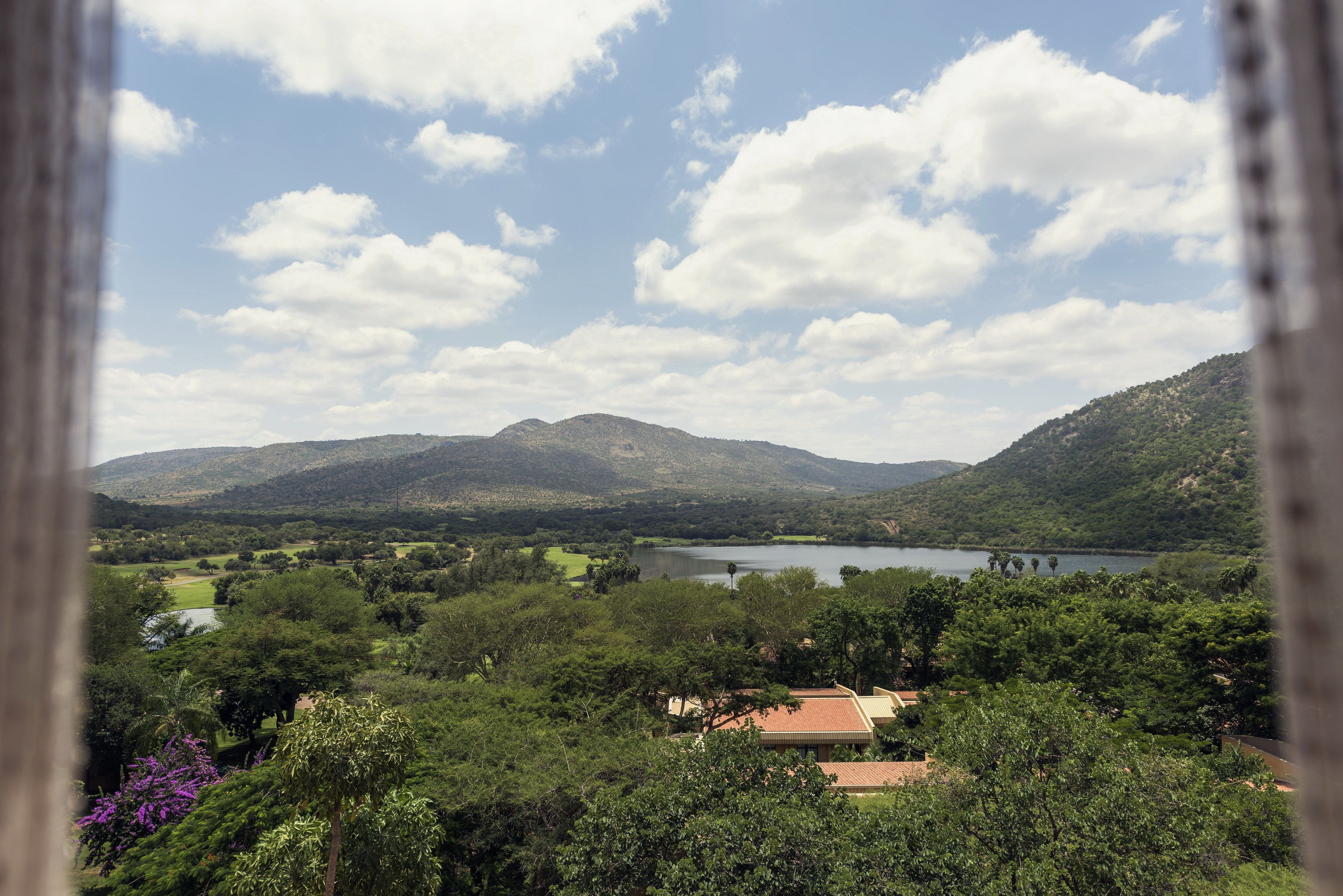A view of a mountainous landscape with a lake, trees, and a building with a red roof.