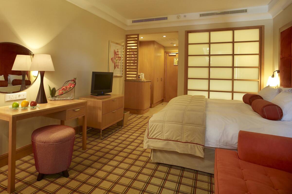 Une chambre d’hôtel avec un lit, un bureau avec un ordinateur, une chaise, une petite table avec des fruits et un miroir.