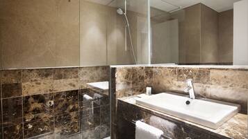Un baño moderno con ducha acristalada, lavamanos blanco y azulejos de mármol.