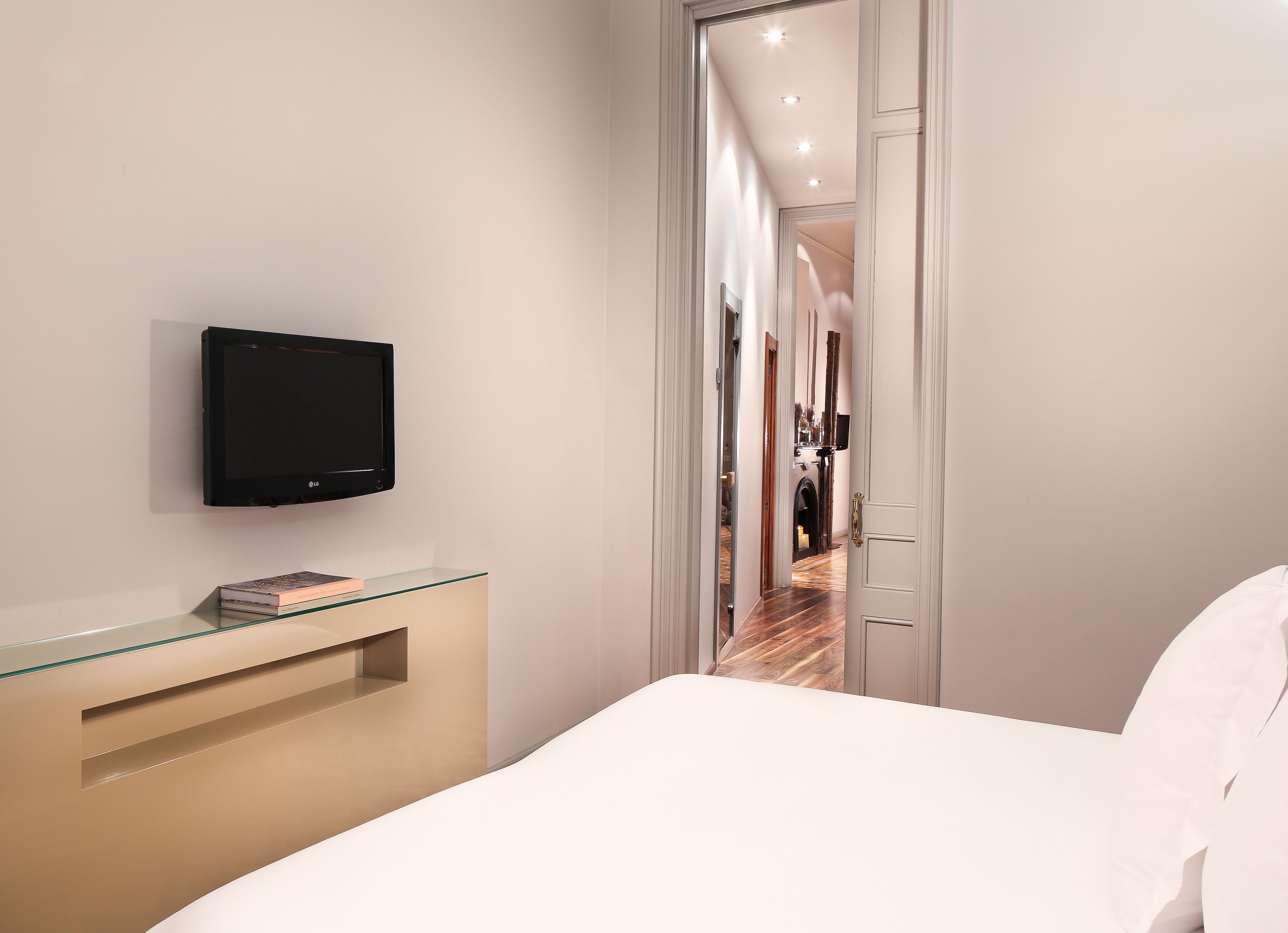 Een moderne hotelkamer met een wandgemonteerde flatscreen televisie, een nachtkastje met glazen blad en een houten vloer.