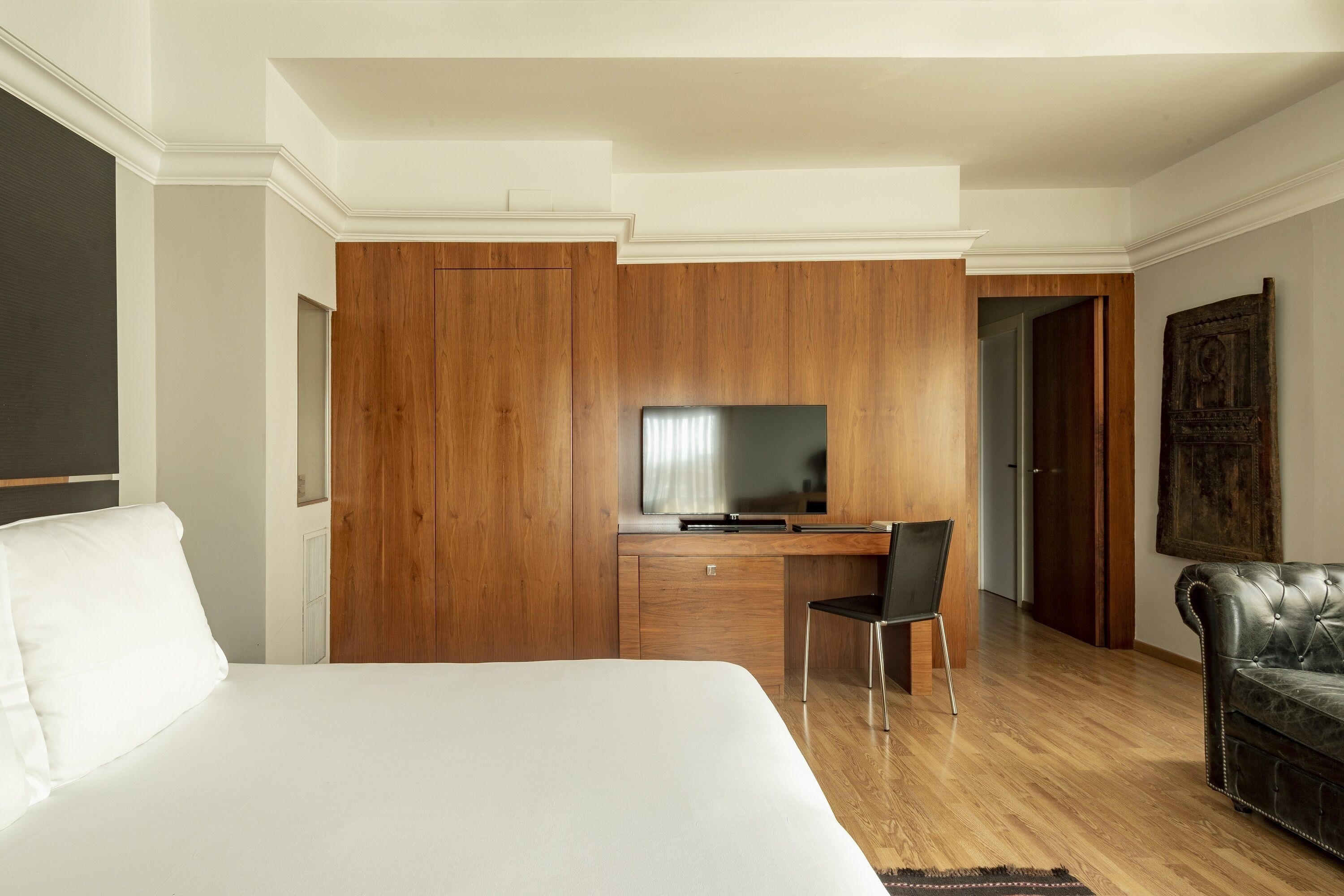 Une chambre d’hôtel avec un grand lit, un bureau en bois avec une télévision, une chaise et un canapé en cuir.