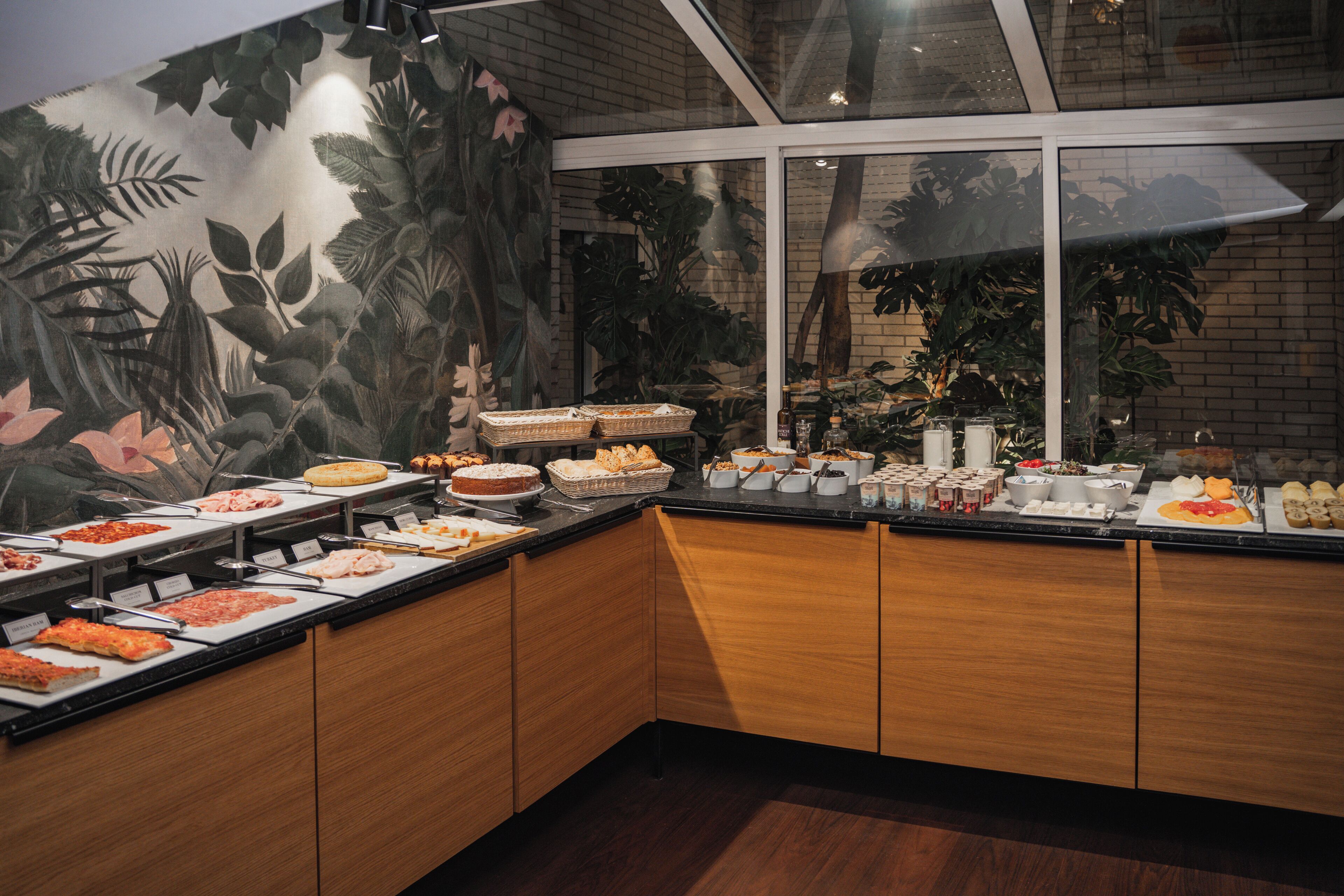 Un bufé con distintos alimentos y un mural tropical de fondo.