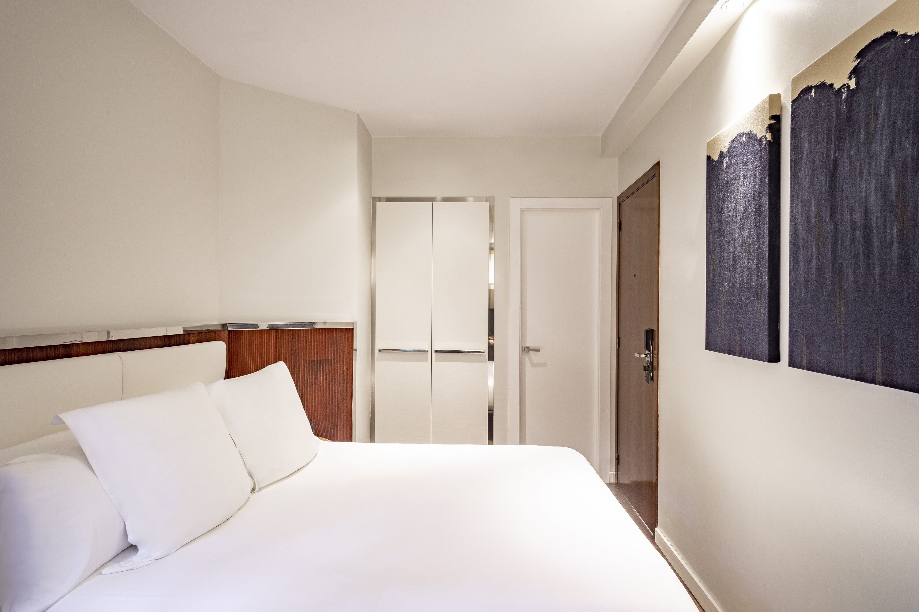 Una habitación de hotel con cama, cabecero de madera, armario y puerta.