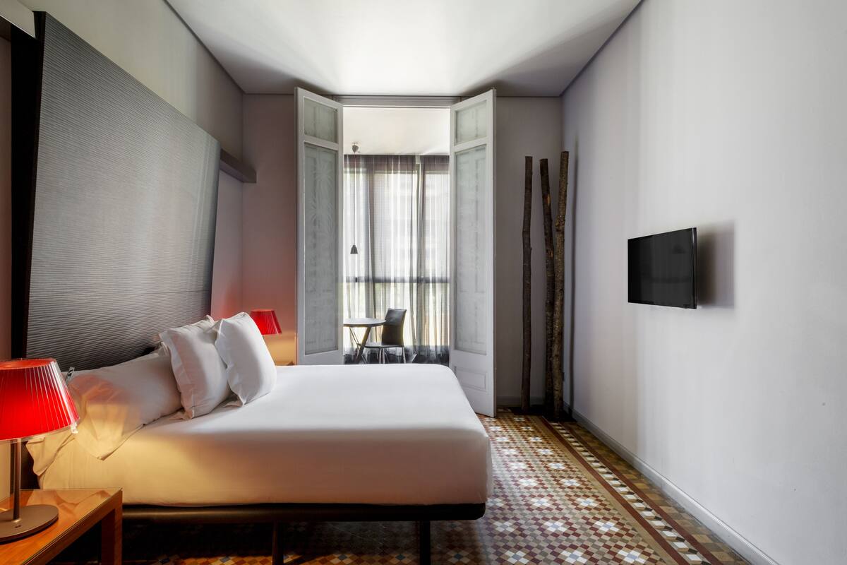 Une chambre d’hôtel avec un lit, une télévision, une lampe, une chaise et une vue sur l’extérieur.