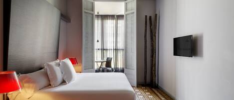 Habitación de hotel con cama, televisión, lámpara, sillón y vista al exterior.