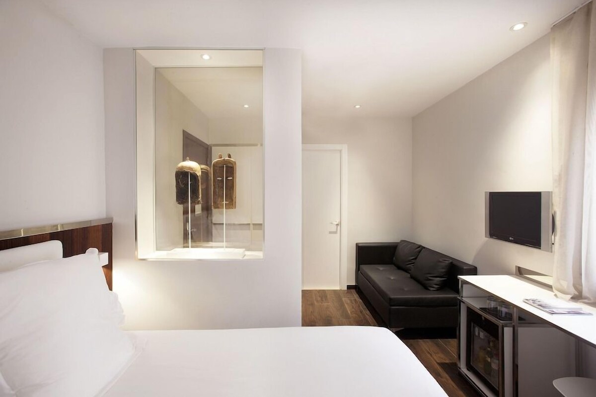 A hotel room with a bed, a sofa, a TV, and a mirror.
