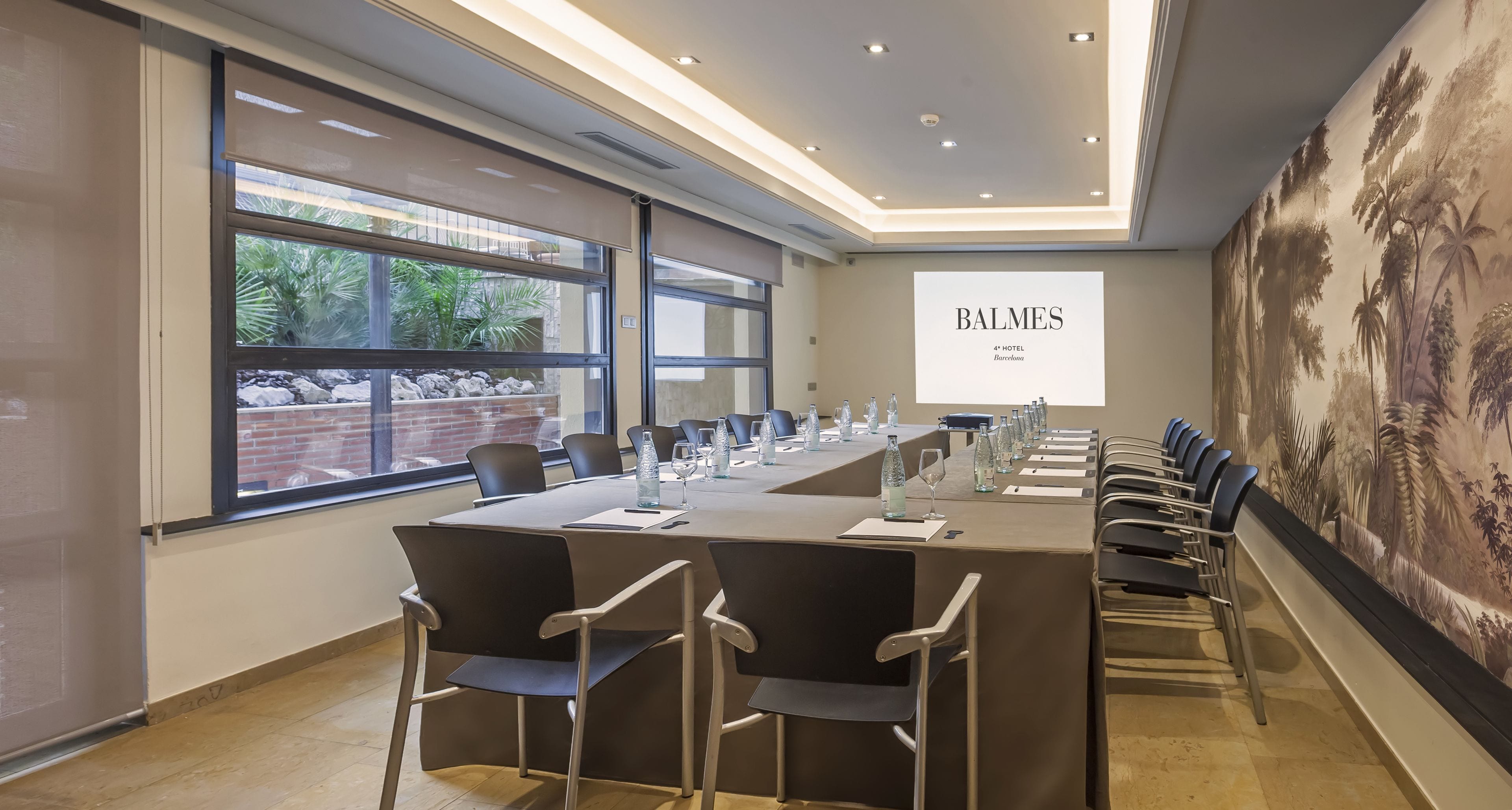 Een vergaderruimte met een lange tafel, stoelen en een projectorscherm waarop 'BALMES 4th HOTEL Barcelona' staat.