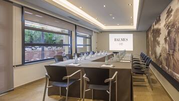 Een vergaderruimte met een lange tafel, stoelen en een projectorscherm waarop 'BALMES 4th HOTEL Barcelona' staat.