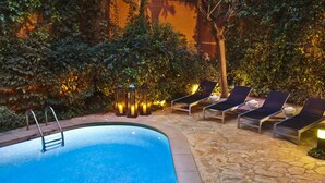 A swimming pool with lounge chairs and candles, surrounded by stone tiles and greenery. - Hotel Balmes, a member of Preferred Hotels & Resorts (Barcelona)