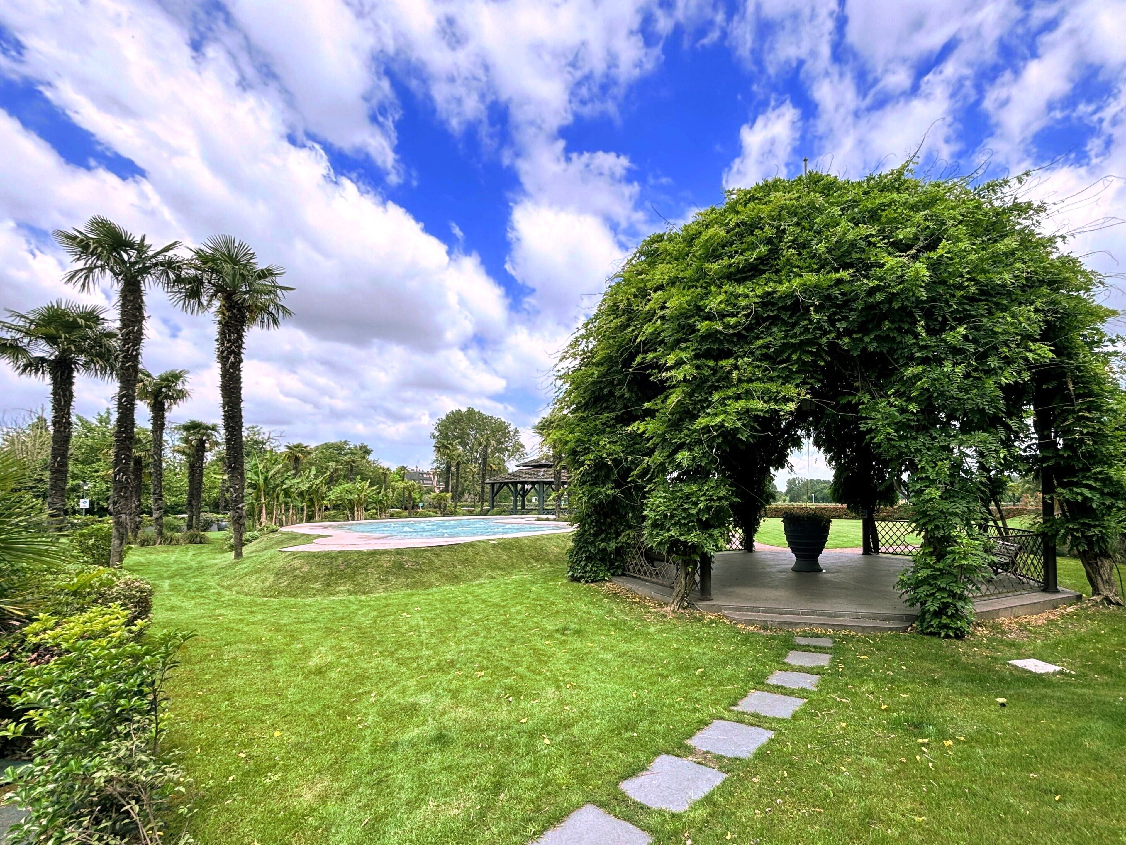 A well-maintained garden with a clear swimming pool, a gazebo, and a variety of trees.