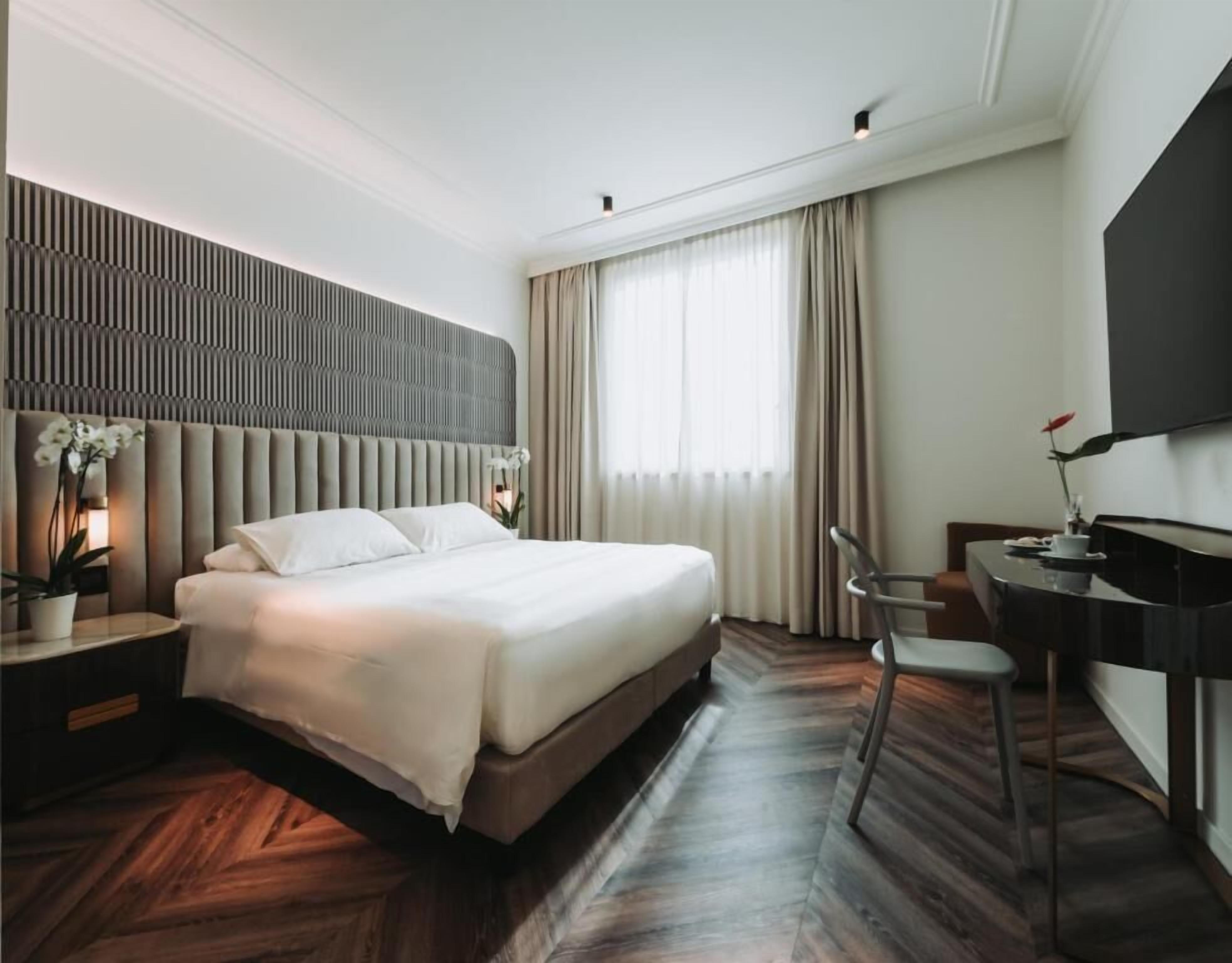 A modern hotel room with a large bed, a desk, and a television.