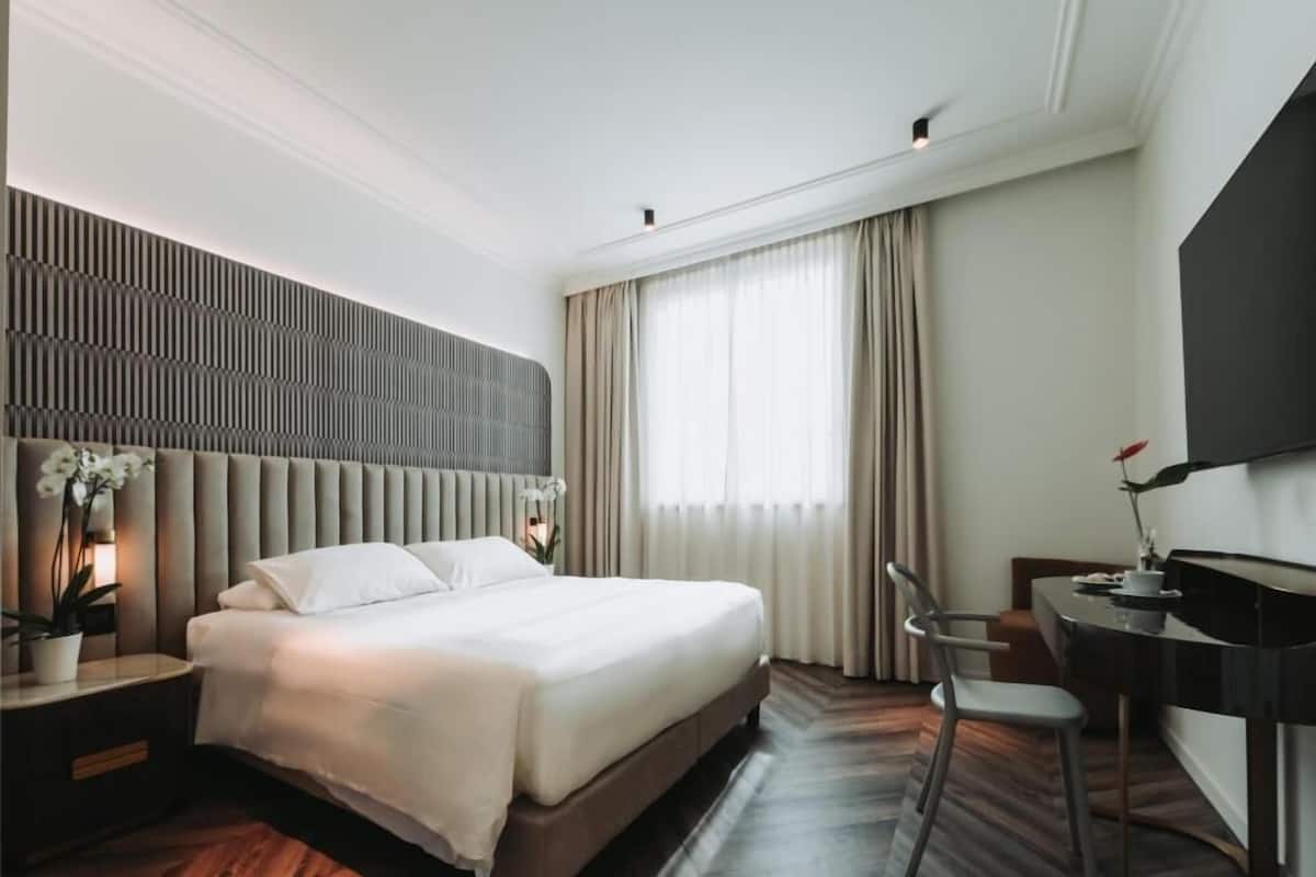 Moderni hotellihuone, jossa on suuri sänky, työpöytä ja televisio.
