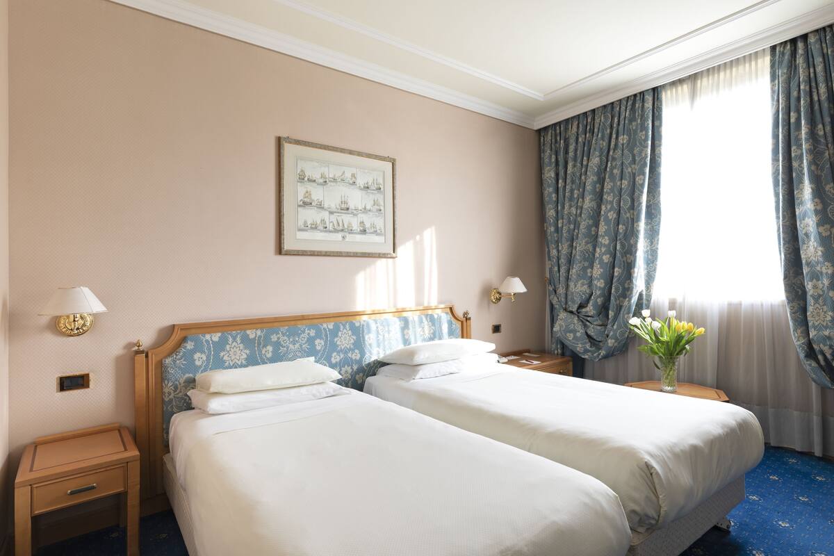 A hotel room with two beds, a framed picture on the wall, and a vase with flowers on the nightstand.