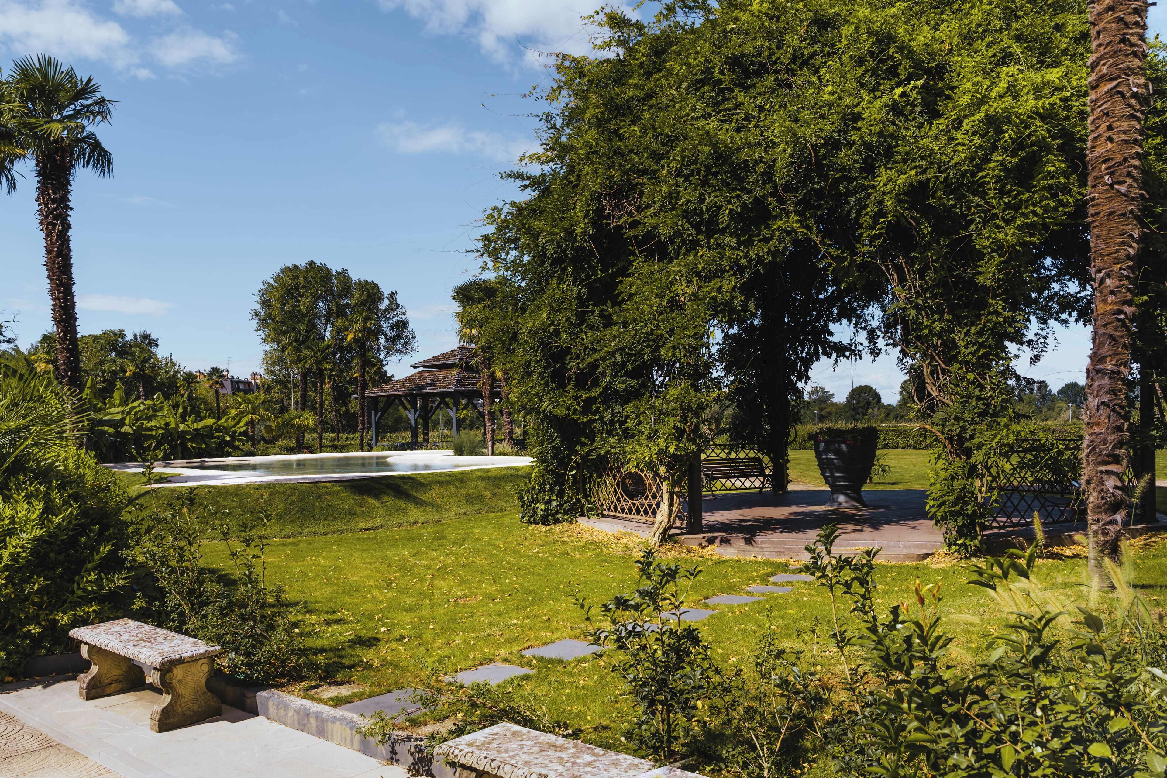 A well-maintained garden with a stone bench, a fountain, and a gazebo.