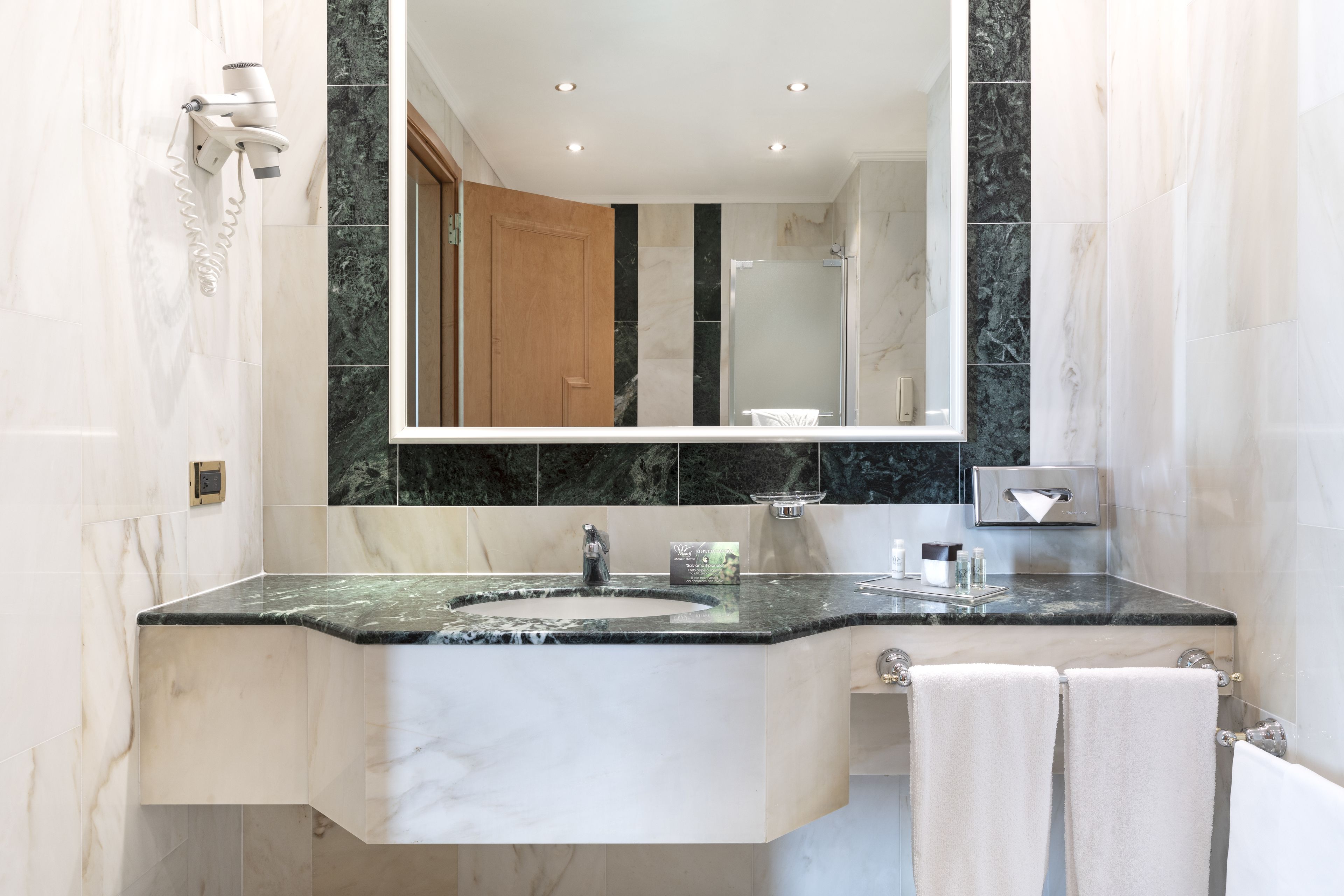 A modern bathroom with a marble sink, a large mirror, and a towel rack.
