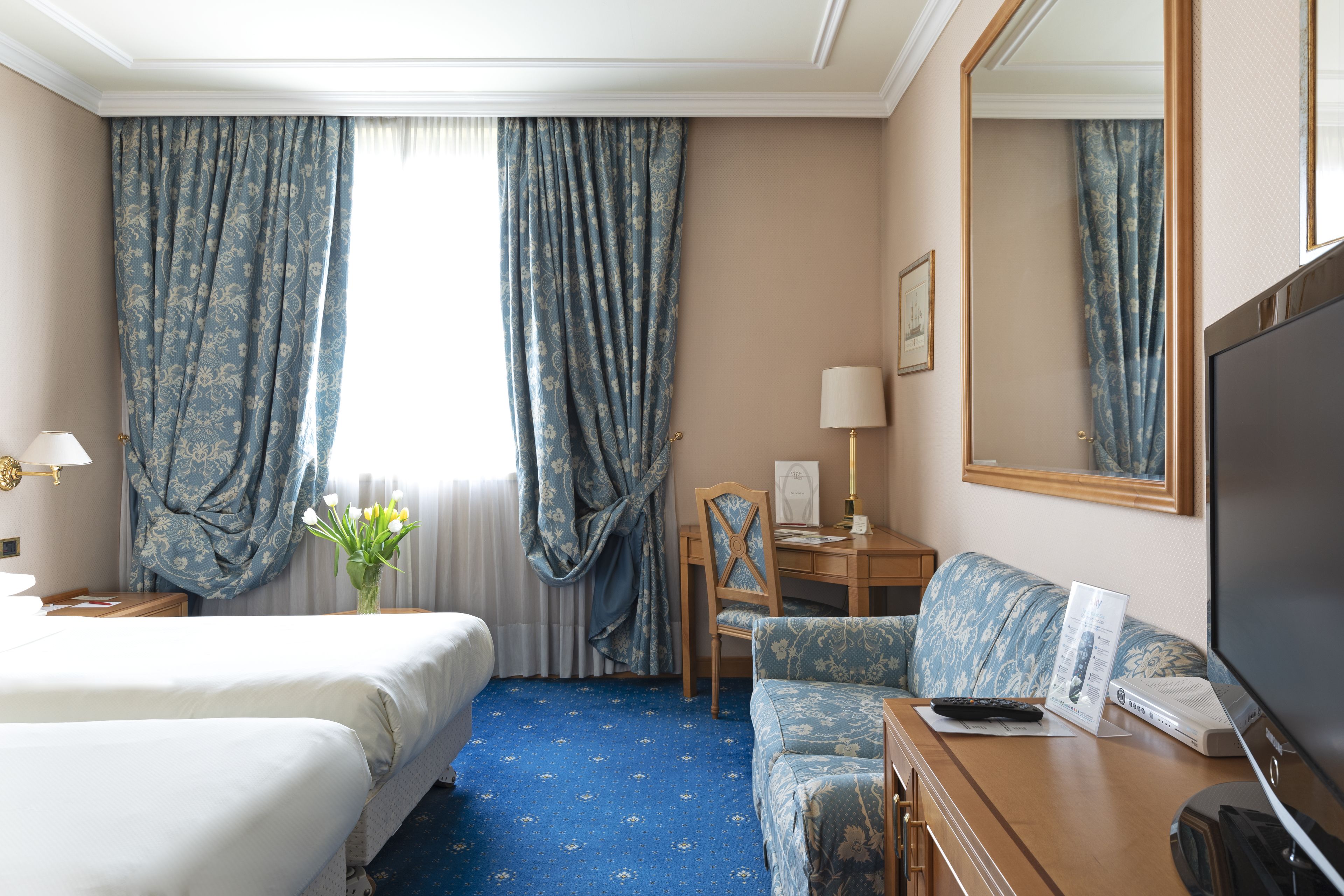 Ein Hotelzimmer mit einem Bett, einem Schreibtisch mit Lampe, einem Sessel, einer Couch und einem Fernseher.