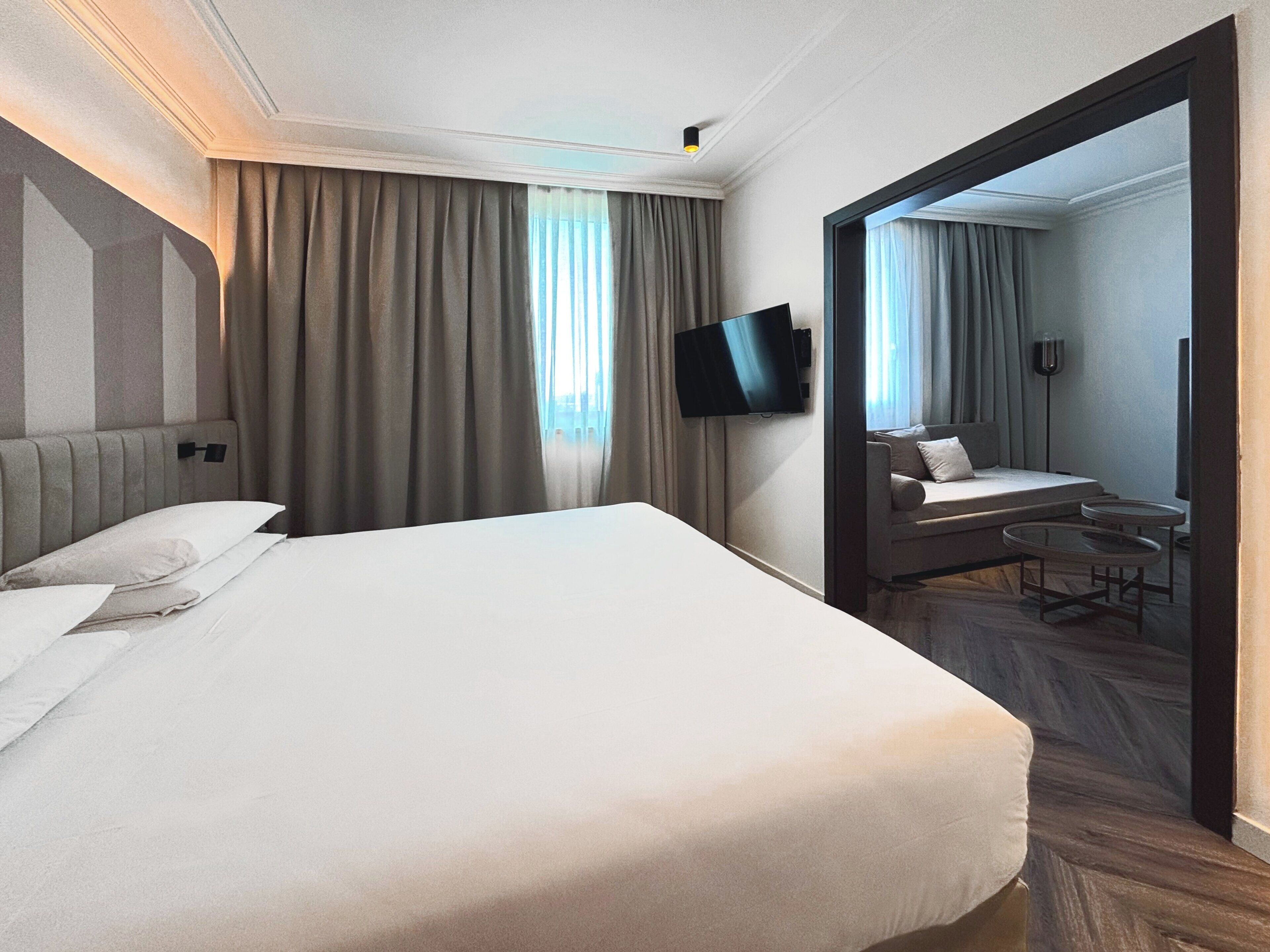 A hotel room with a large bed, a flat-screen TV mounted on the wall, and a small seating area with a table and chairs.