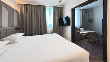 A hotel room with a large bed, a flat-screen TV mounted on the wall, and a small seating area with a table and chairs.