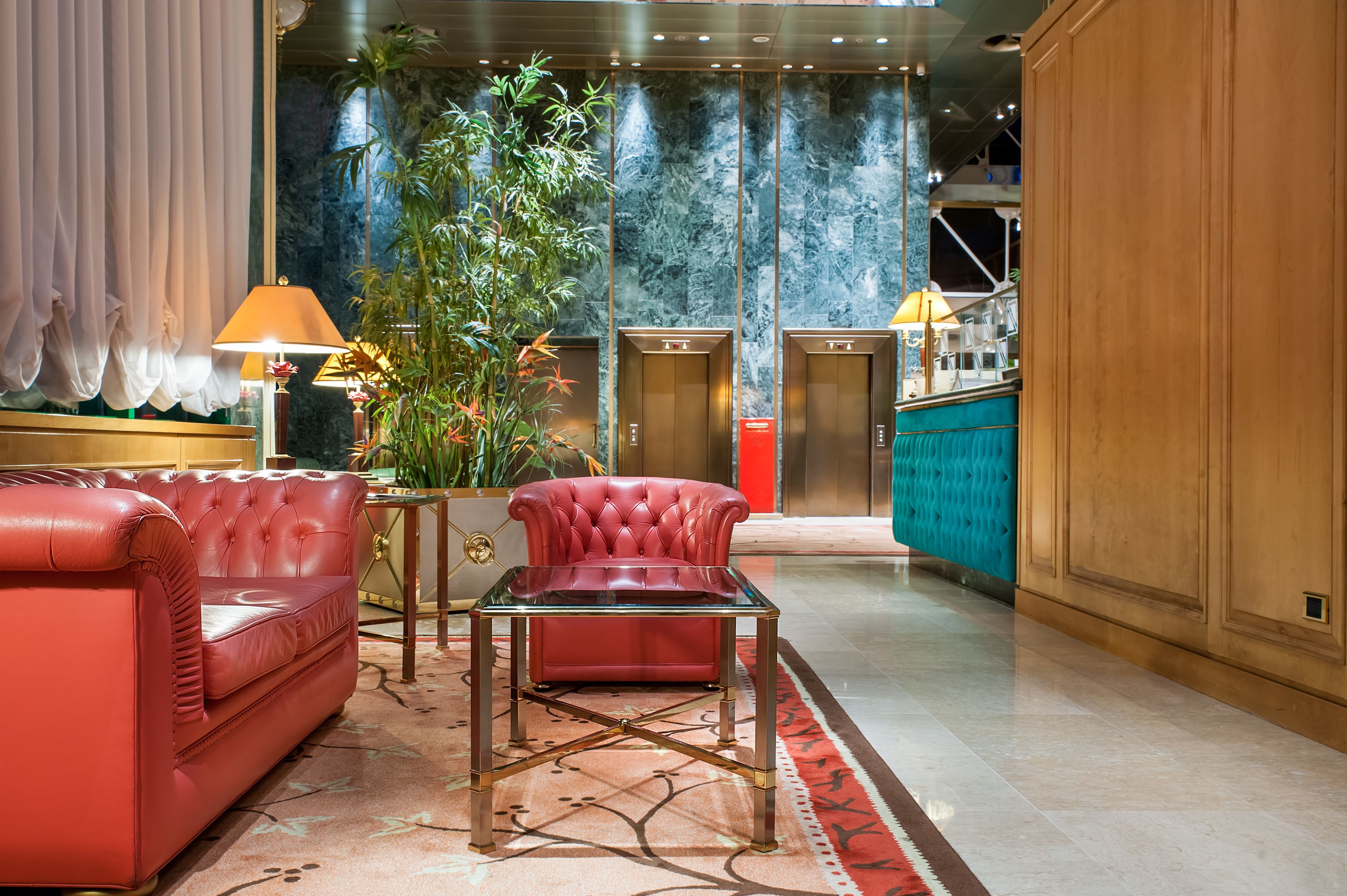 Eine moderne Lobby mit einem roten Ledersofa, einem Glastisch und einer großen Pflanze in einem Topf.