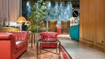 A modern lobby with a red leather sofa, a glass coffee table, and a large potted plant.