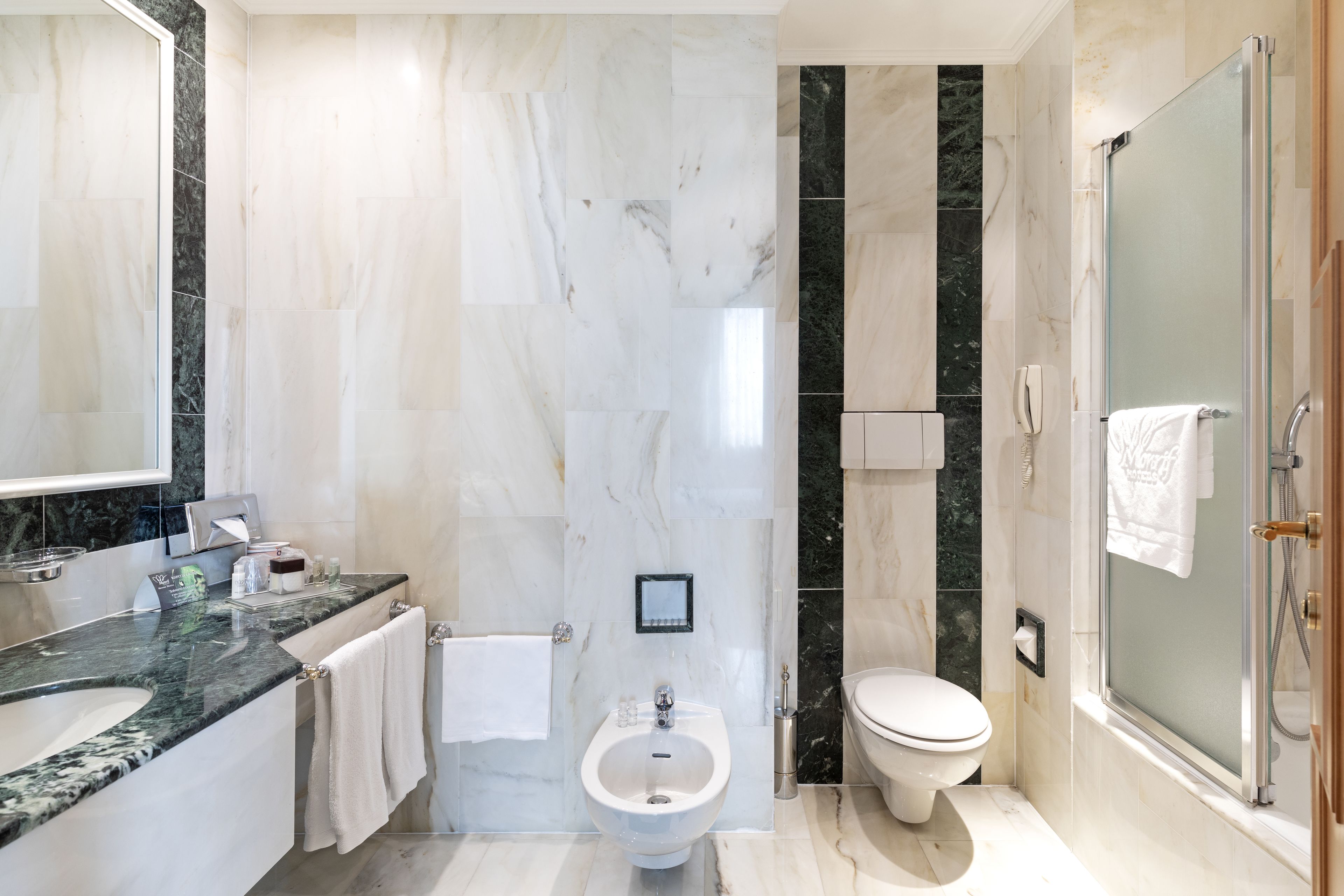 Un baño moderno con tocador de mármol, un bidé, inodoro y ducha con mampara de vidrio.
