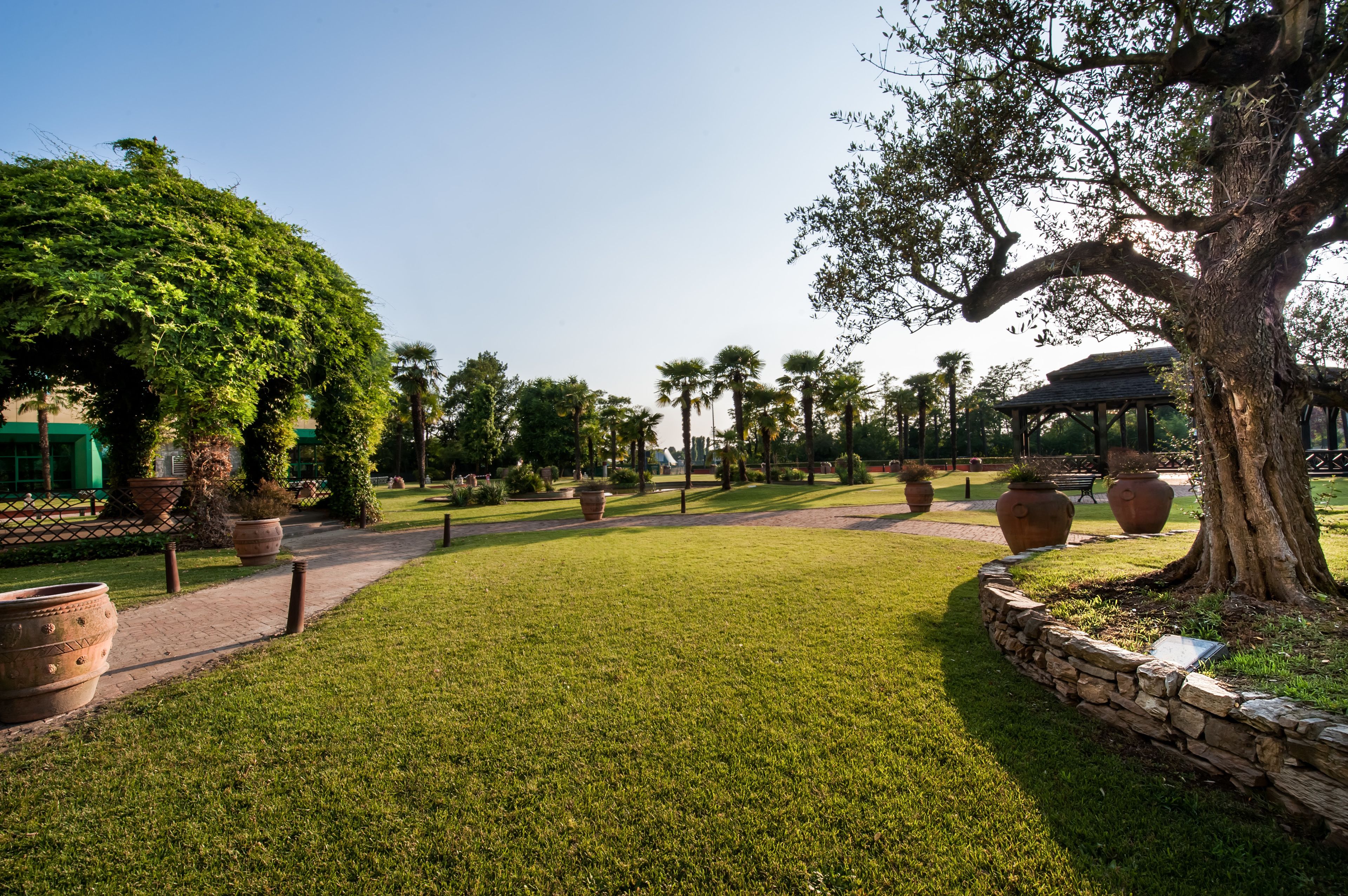 Un jardin bien entretenu, avec un chemin dallé, de grands pots en terre cuite et un kiosque en arrière-plan.