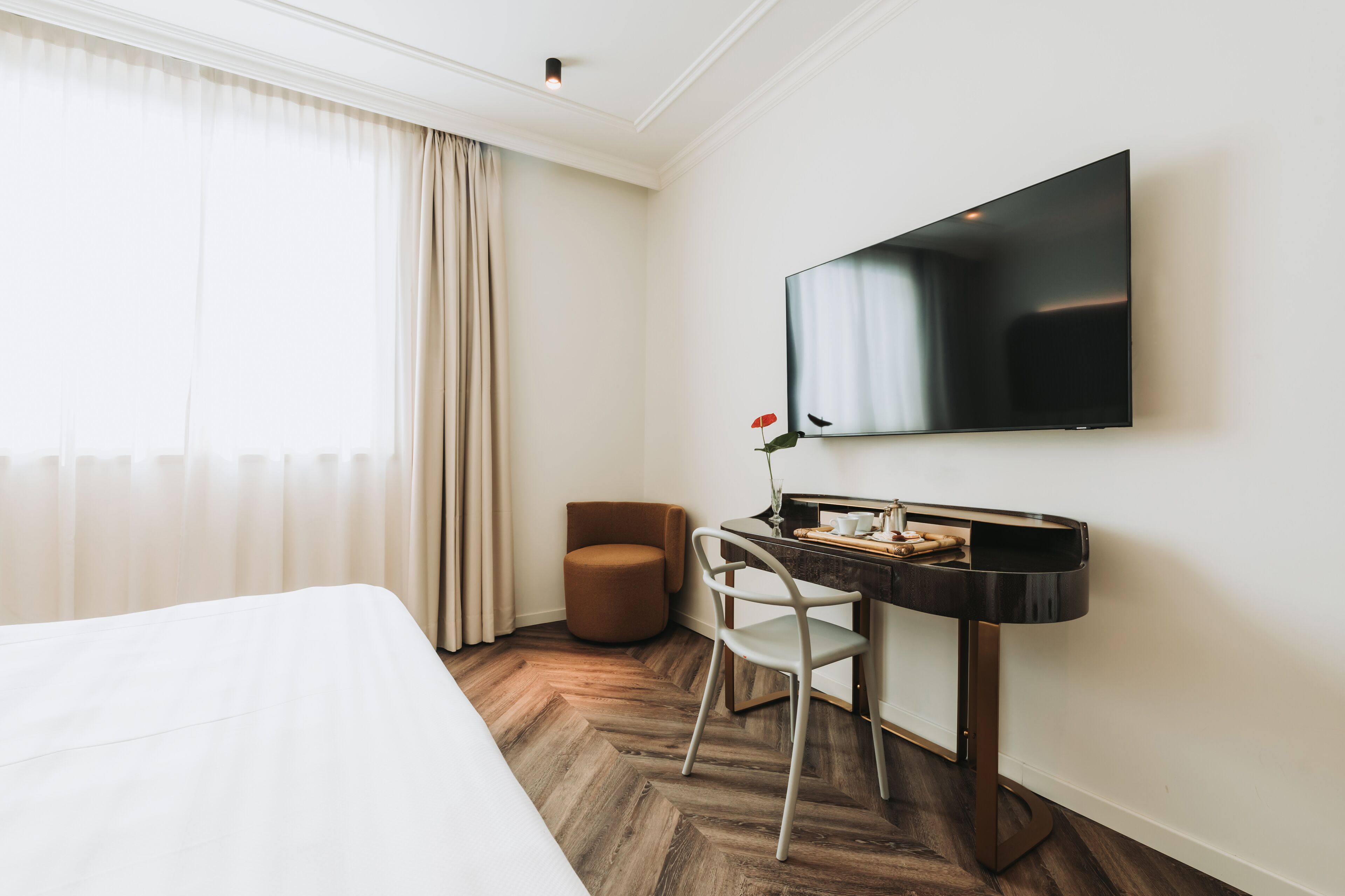 Habitación de hotel con cama, escritorio con silla, televisión de pantalla plana y ventana con cortinas.