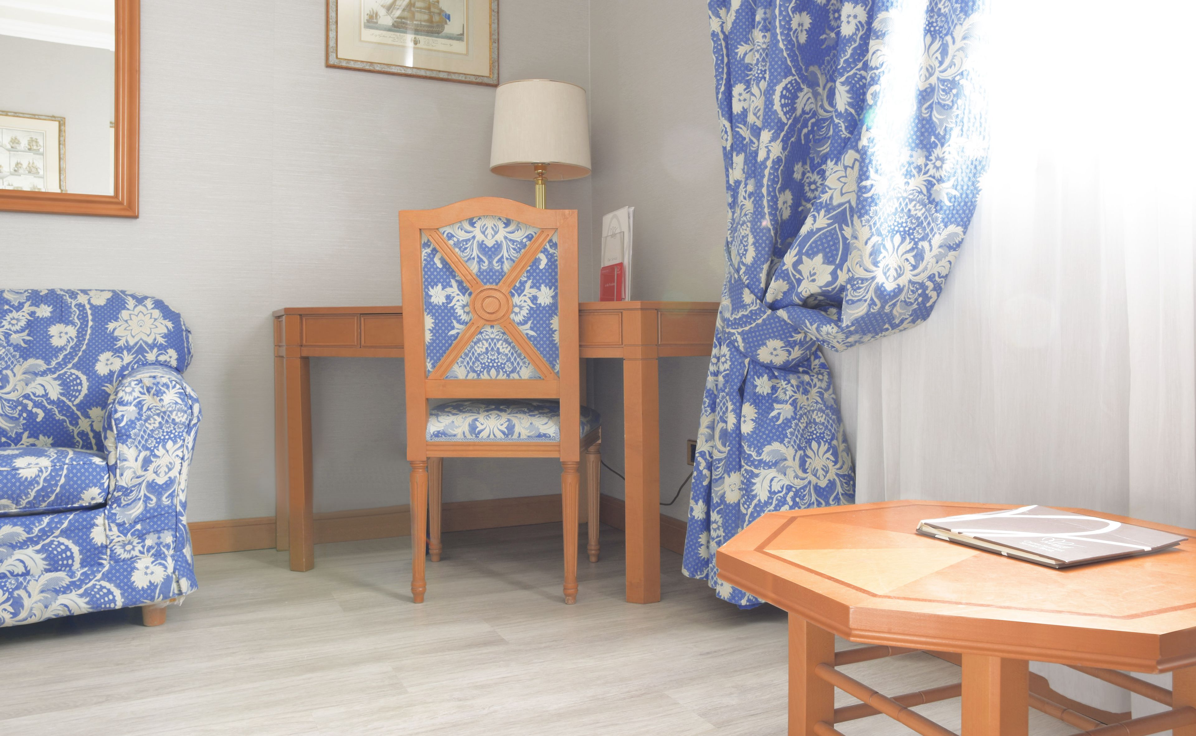 A room with a wooden desk, a chair, a table, and a lamp.