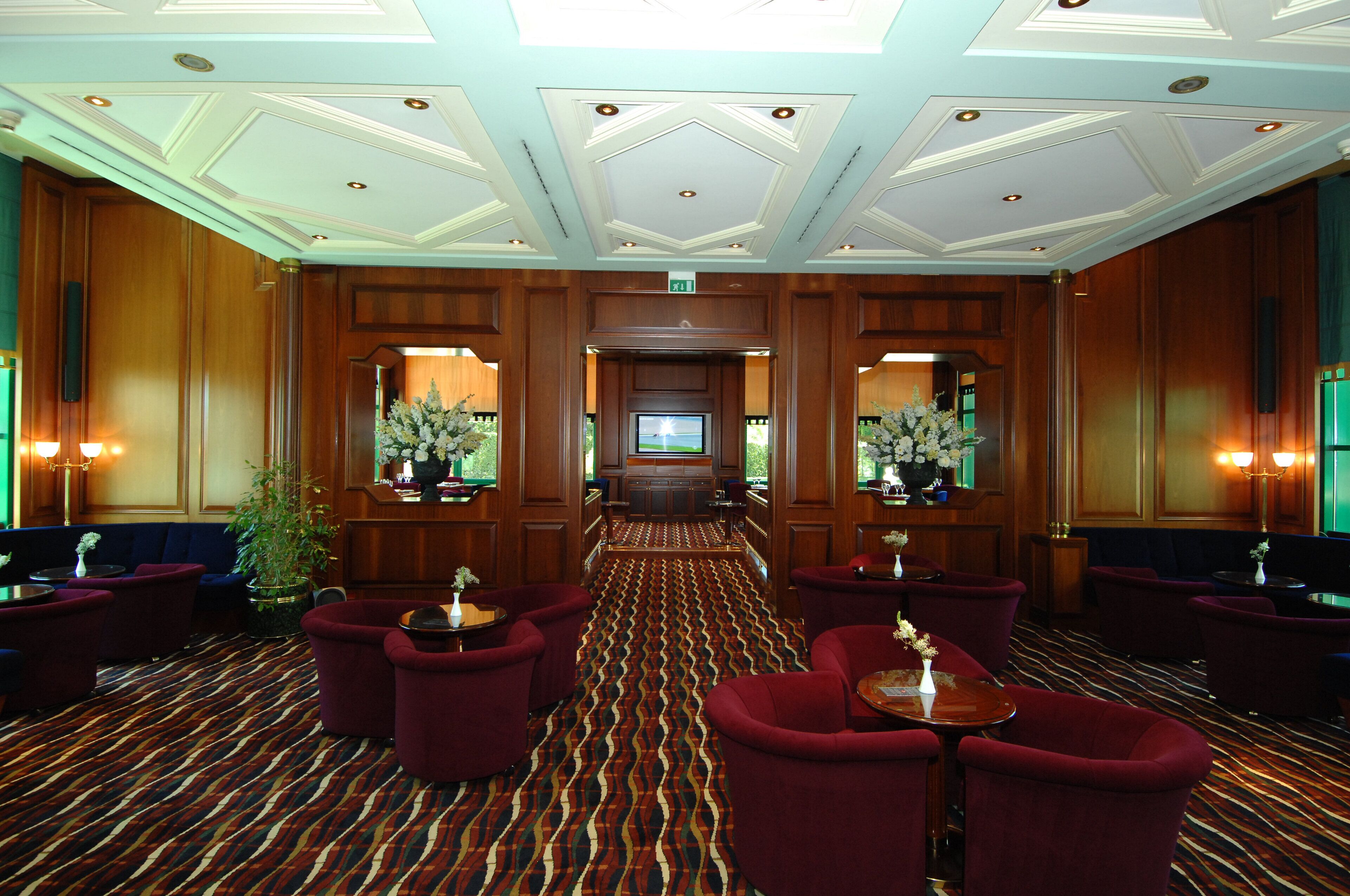 Eine Hotellobby mit einem gemusterten Teppich, roten Polstersitzmöglichkeiten, einem Fernseher und einer Rezeption.