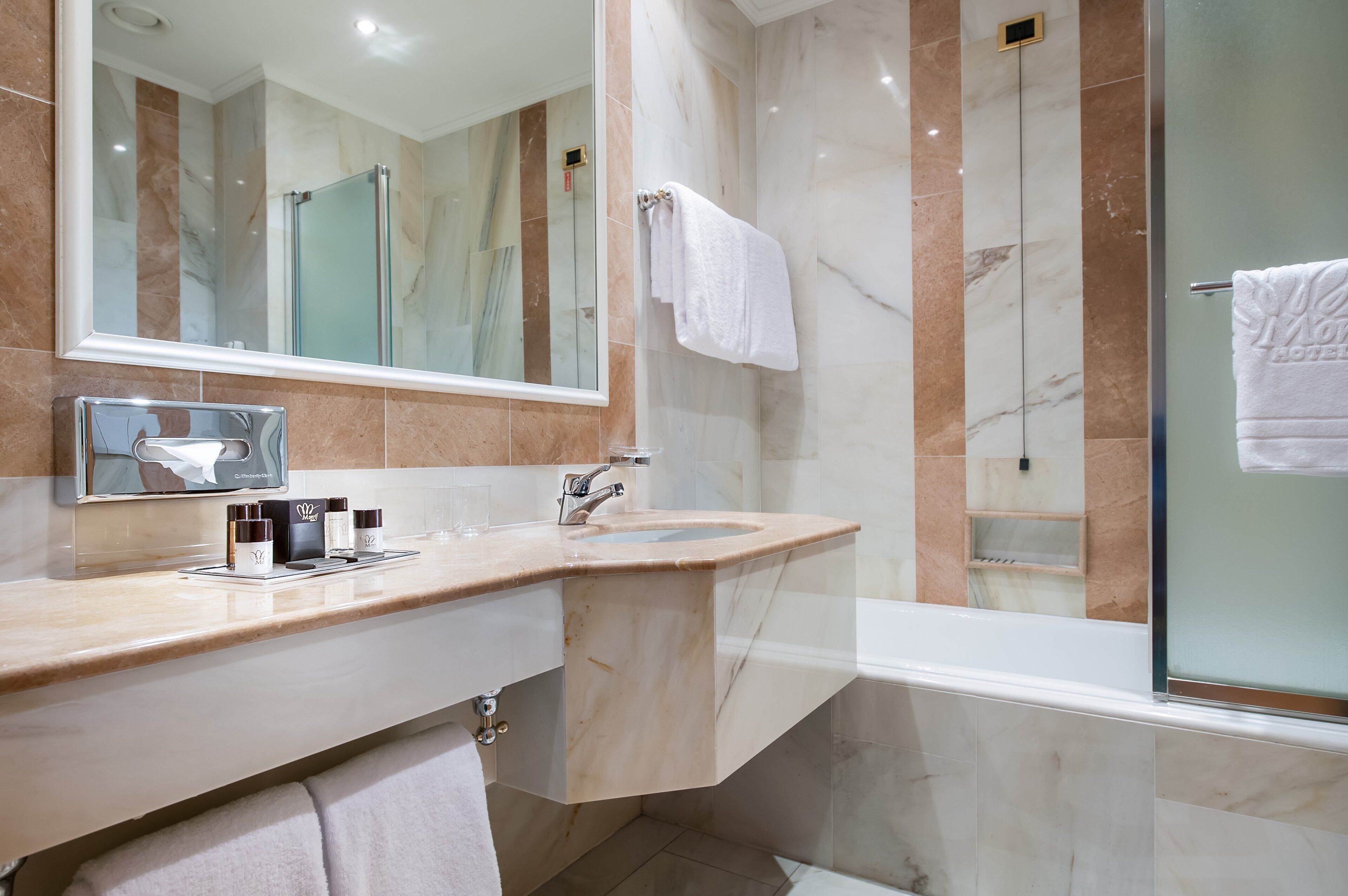 Un baño moderno con tocador de mármol, cabina de ducha con mampara de vidrio y un espejo grande.