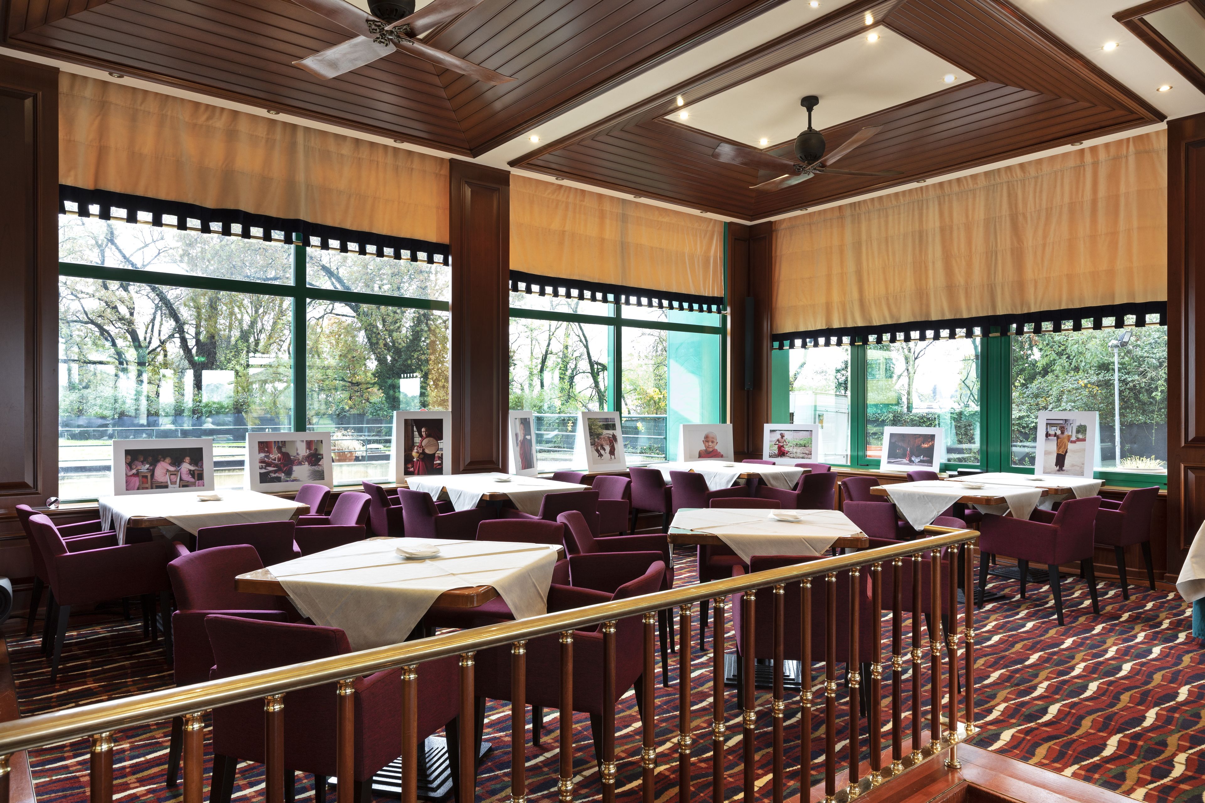 A restaurant with multiple tables and chairs, large windows with views of trees, and a patterned carpet.