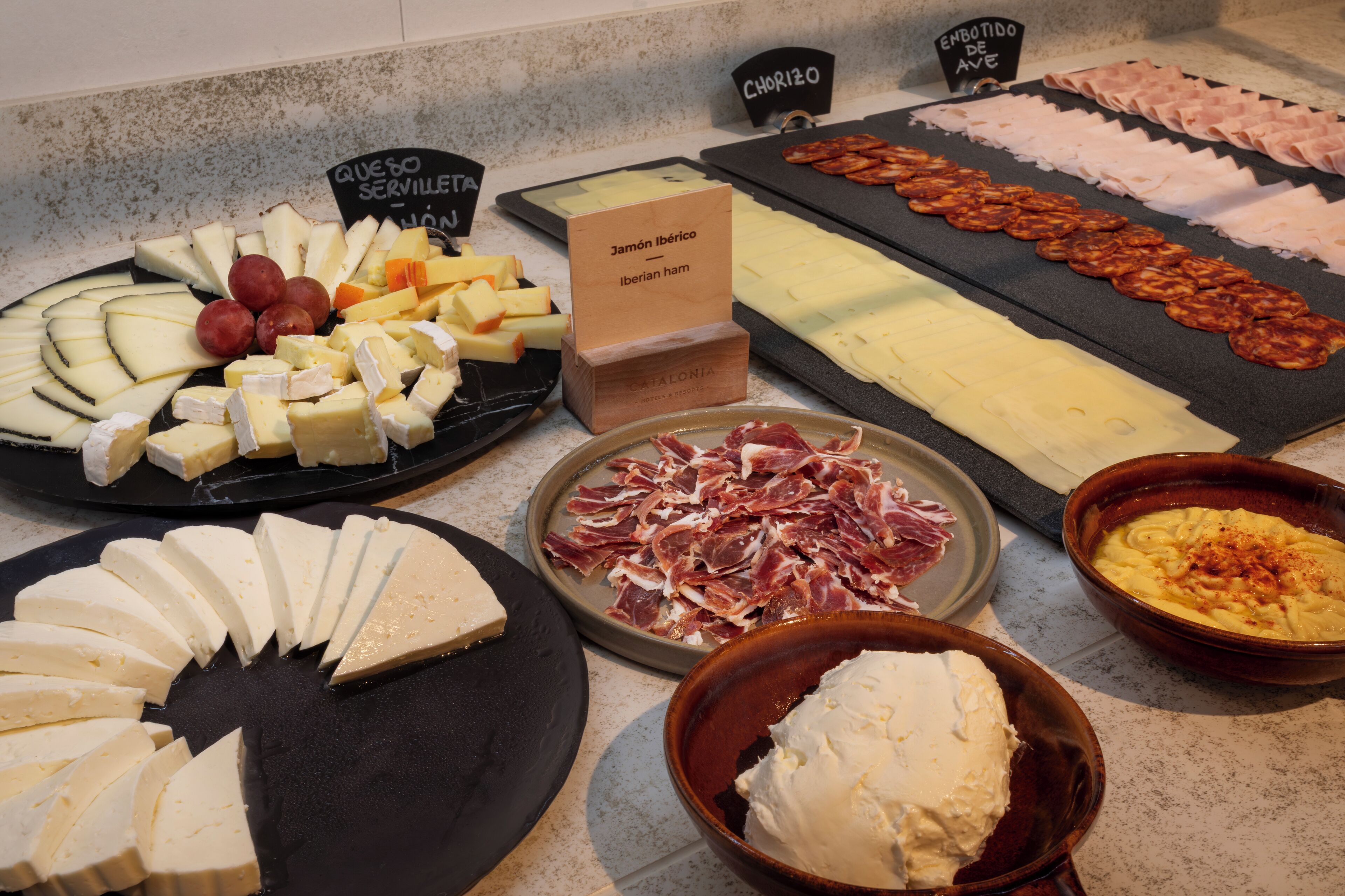 A variety of cheeses, cured meats, and a bowl of dip on a counter.