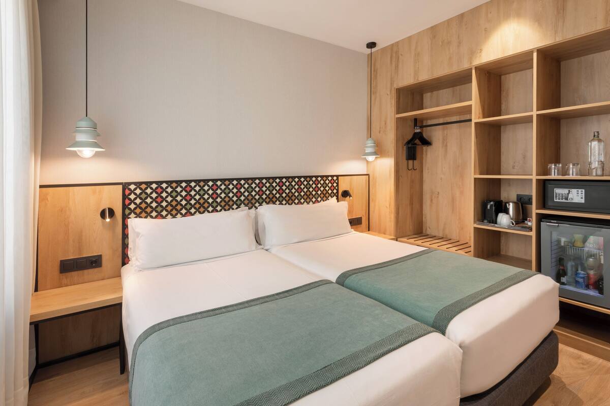 A double bed with a geometric-patterned headboard, bedside tables, a wardrobe, and a minibar.