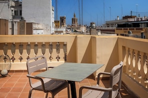 Una terraza con mesa y sillas, una cerca decorativa y vista a edificios y una torre al fondo.